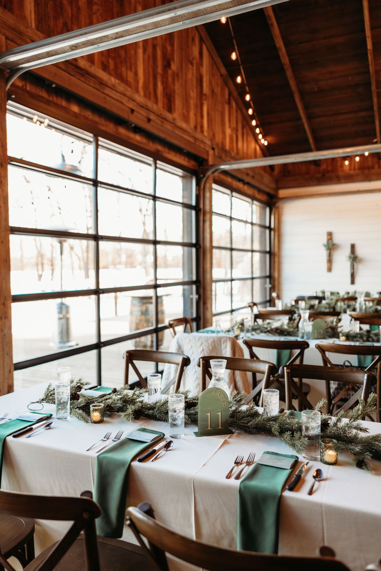 Rustic barn wedding reception venue with long tables set with white linens and teal accents near large windows.