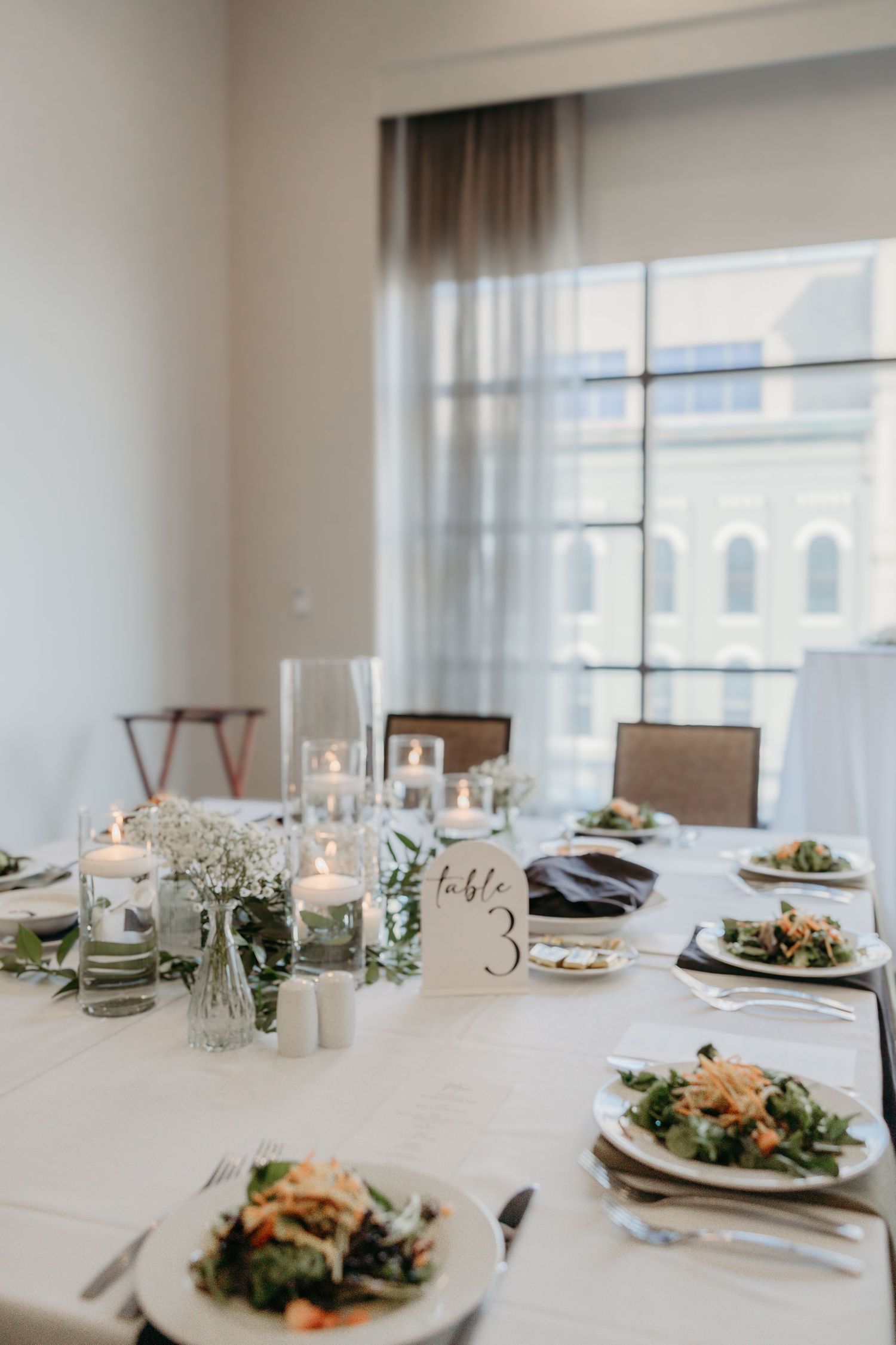 Elegant table setting with plated salads, glass candle holders and baby's breath centerpieces in a bright dining room.