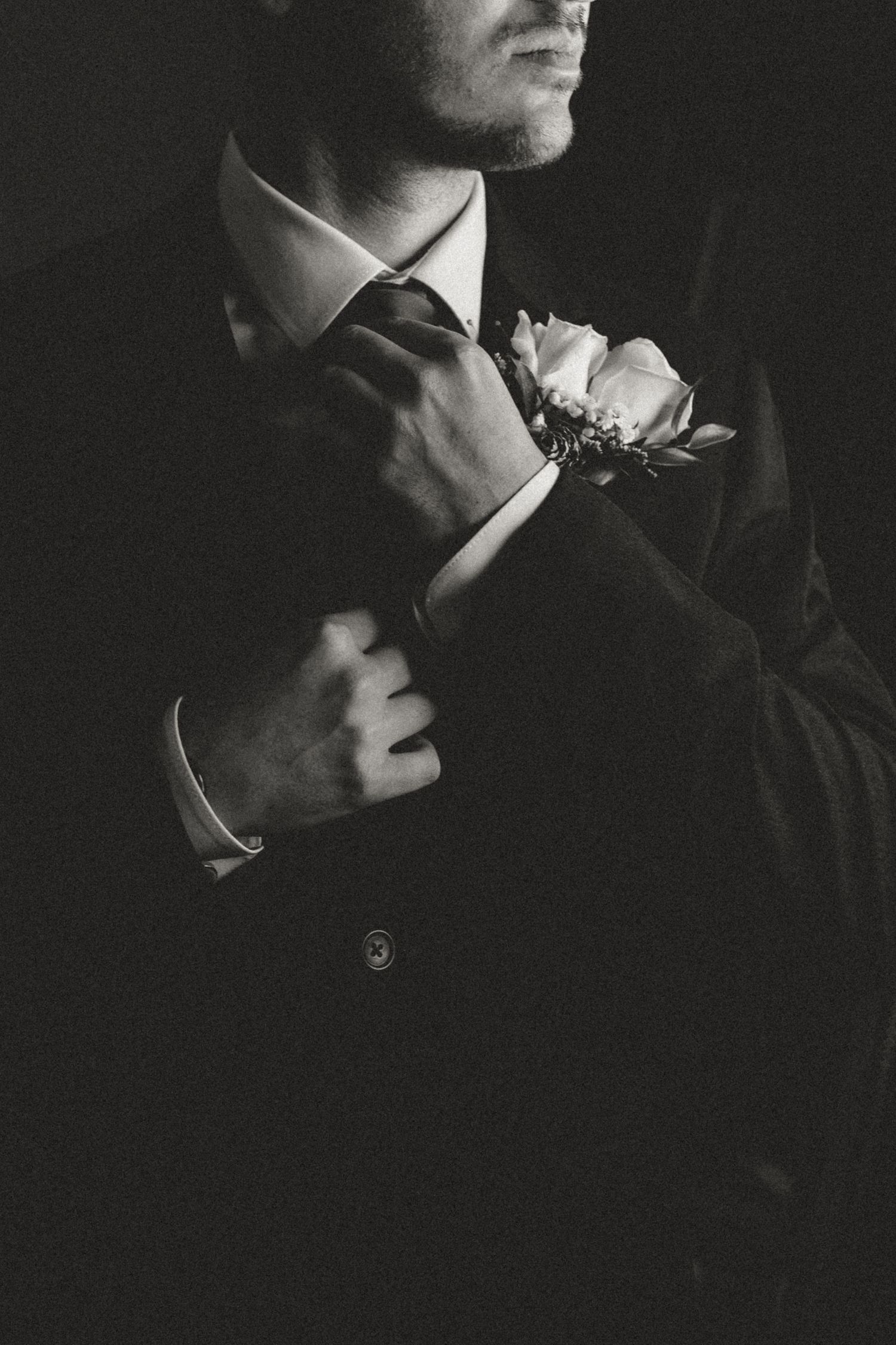 A black and white close-up photograph of a person wearing formal wedding attire with a boutonniere.