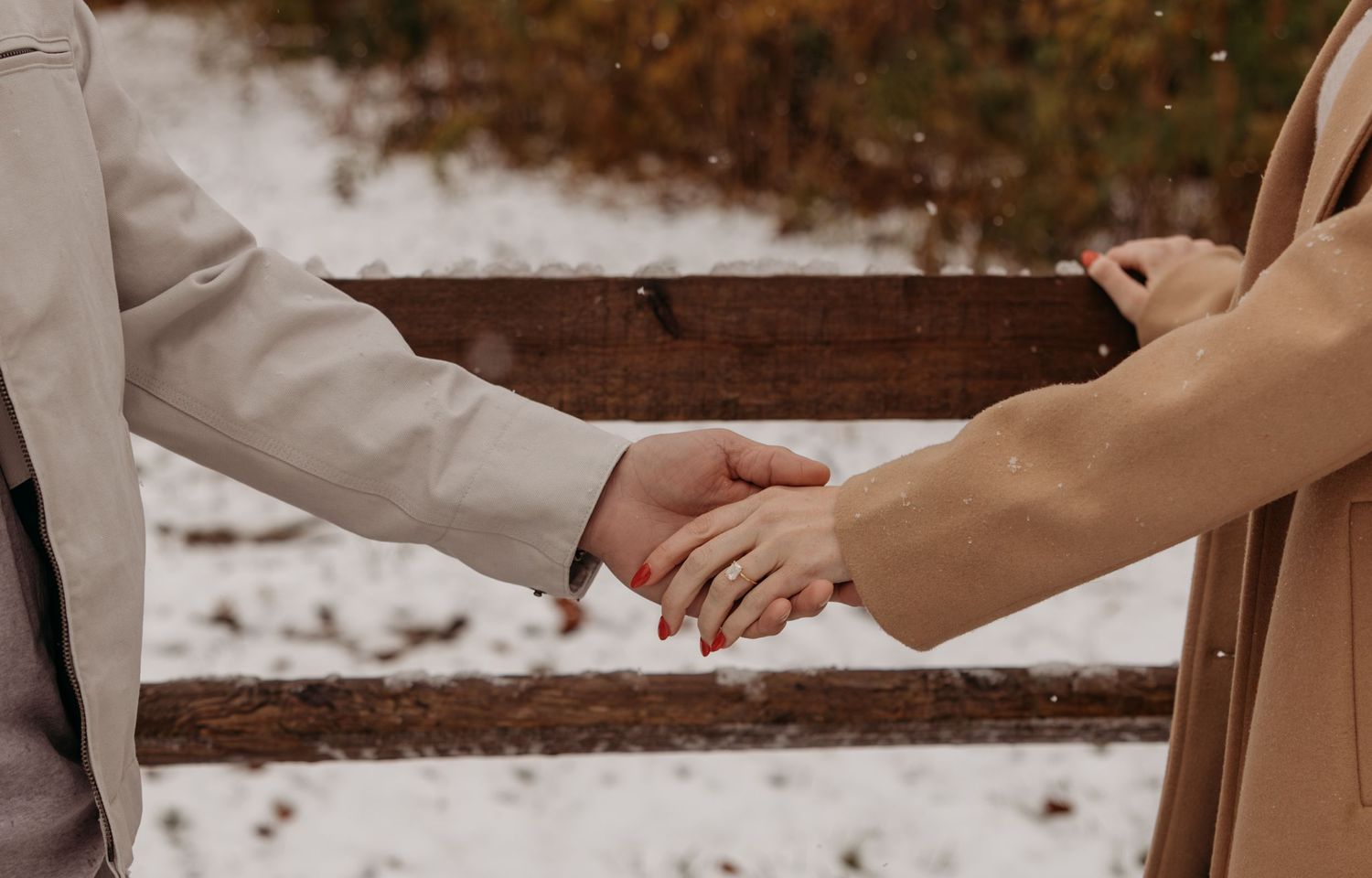 Close-up of hands holding each other tenderly against a snowy winter background.