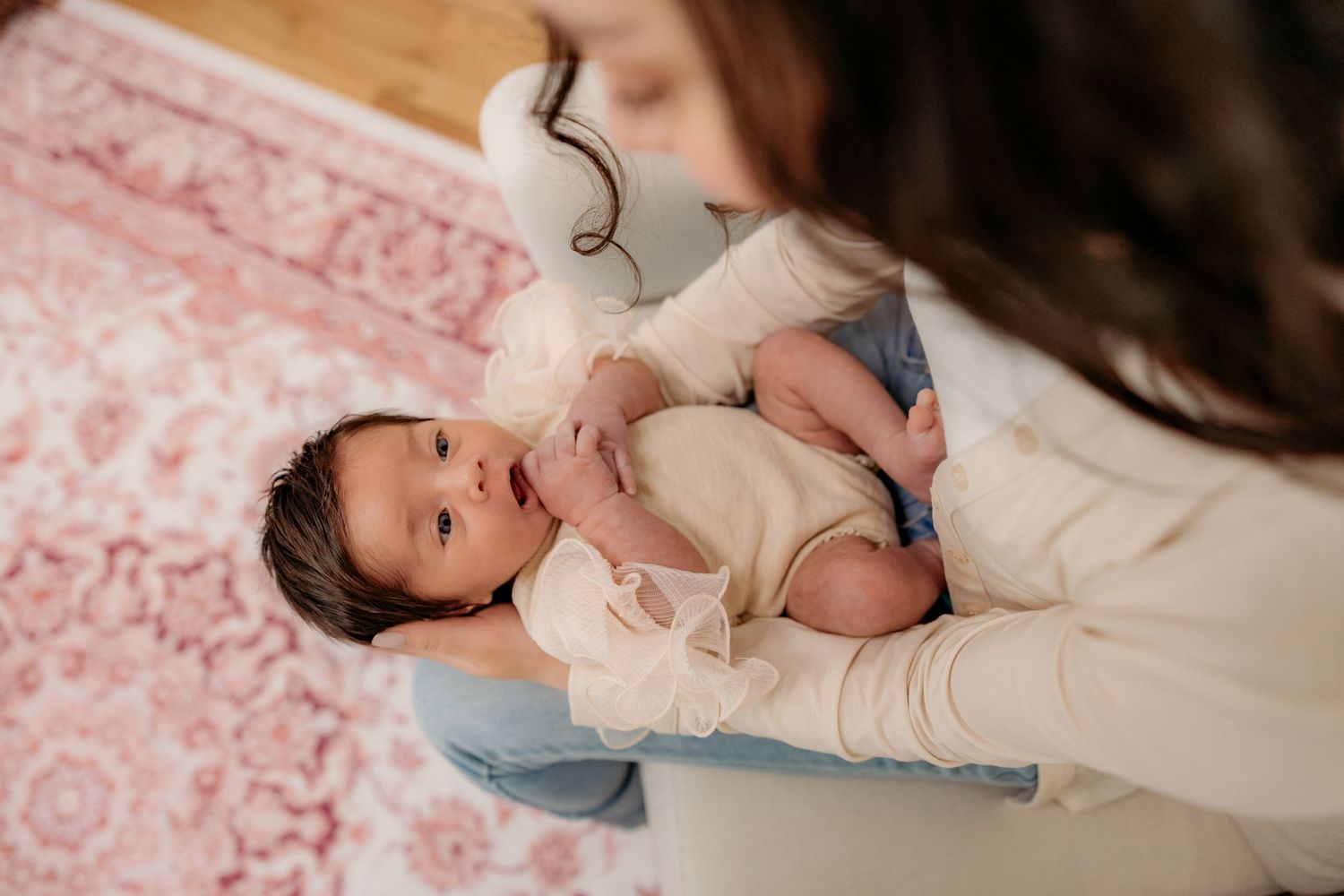 A baby in light clothing lying on a pink floral patterned blanket.