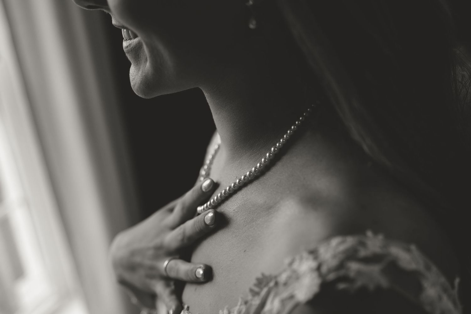 A black and white closeup photograph captures someone wearing jewelry and formal attire in a soft, romantic style.