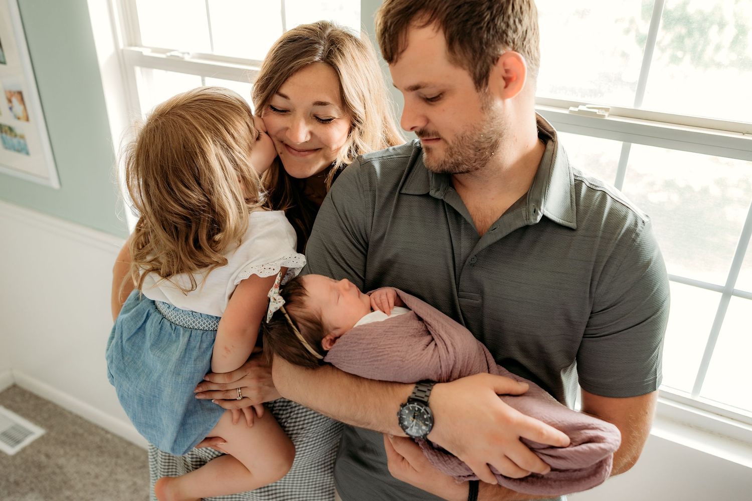 A joyful family moment shared by a window in their home while holding their newborn baby.