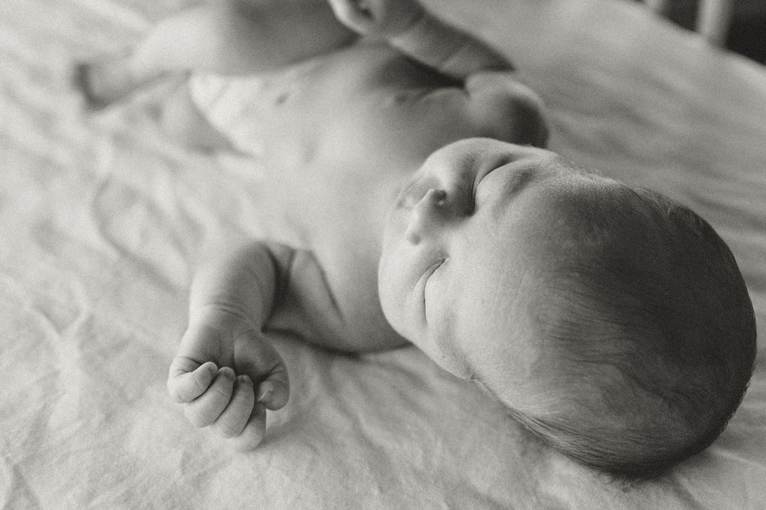 Sweet sleeping baby rests peacefully on soft white bedding in black and white photograph.