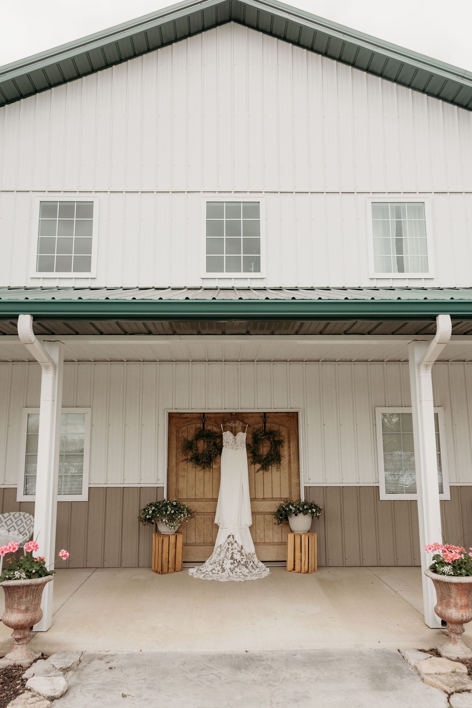 A white wedding dress hangs on display at the entrance of a farmhouse style venue with green trim and rustic decorations.