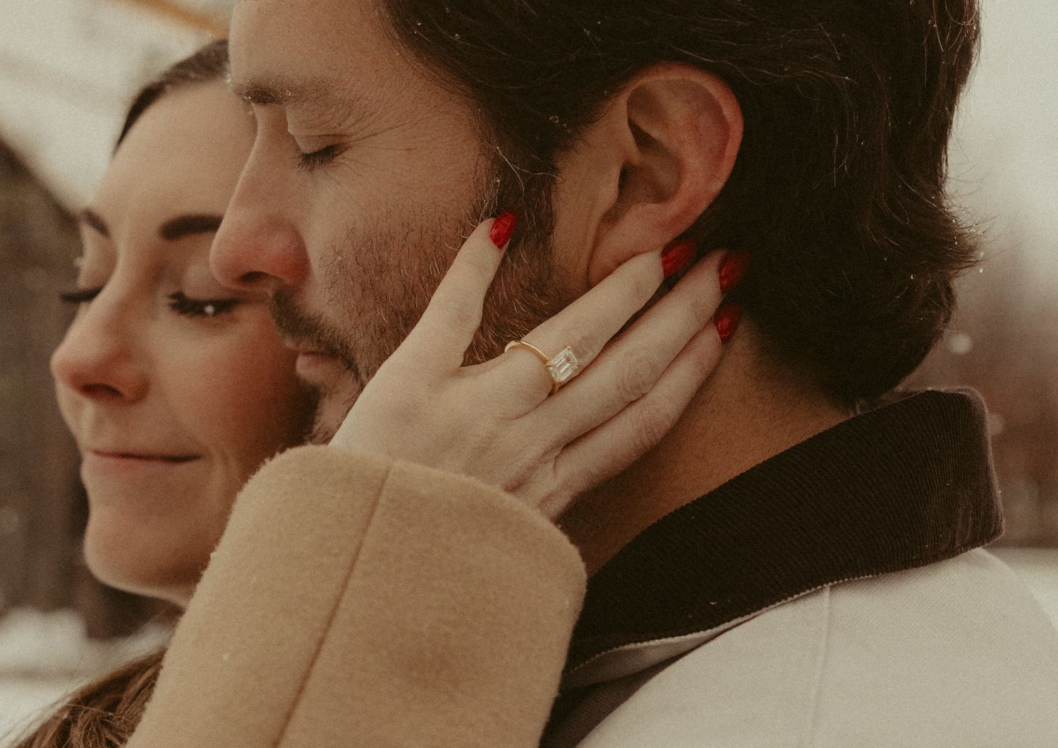 Two people sharing an intimate moment with hands touching faces in a warm-toned photograph.
