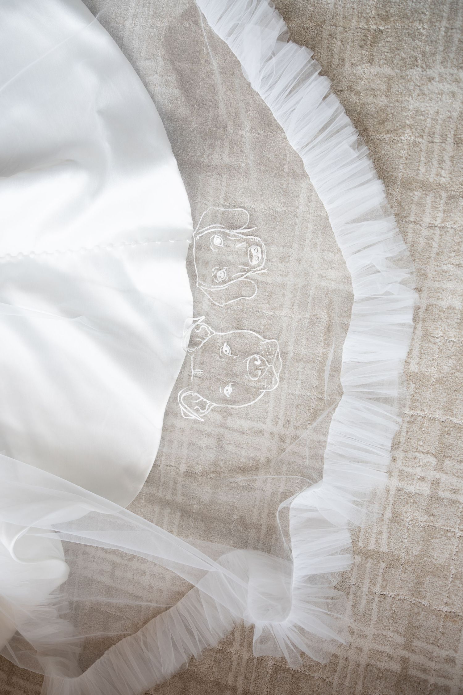 White tulle wedding veil with delicate embroidered floral details and ruffled edge laid flat on linen surface.