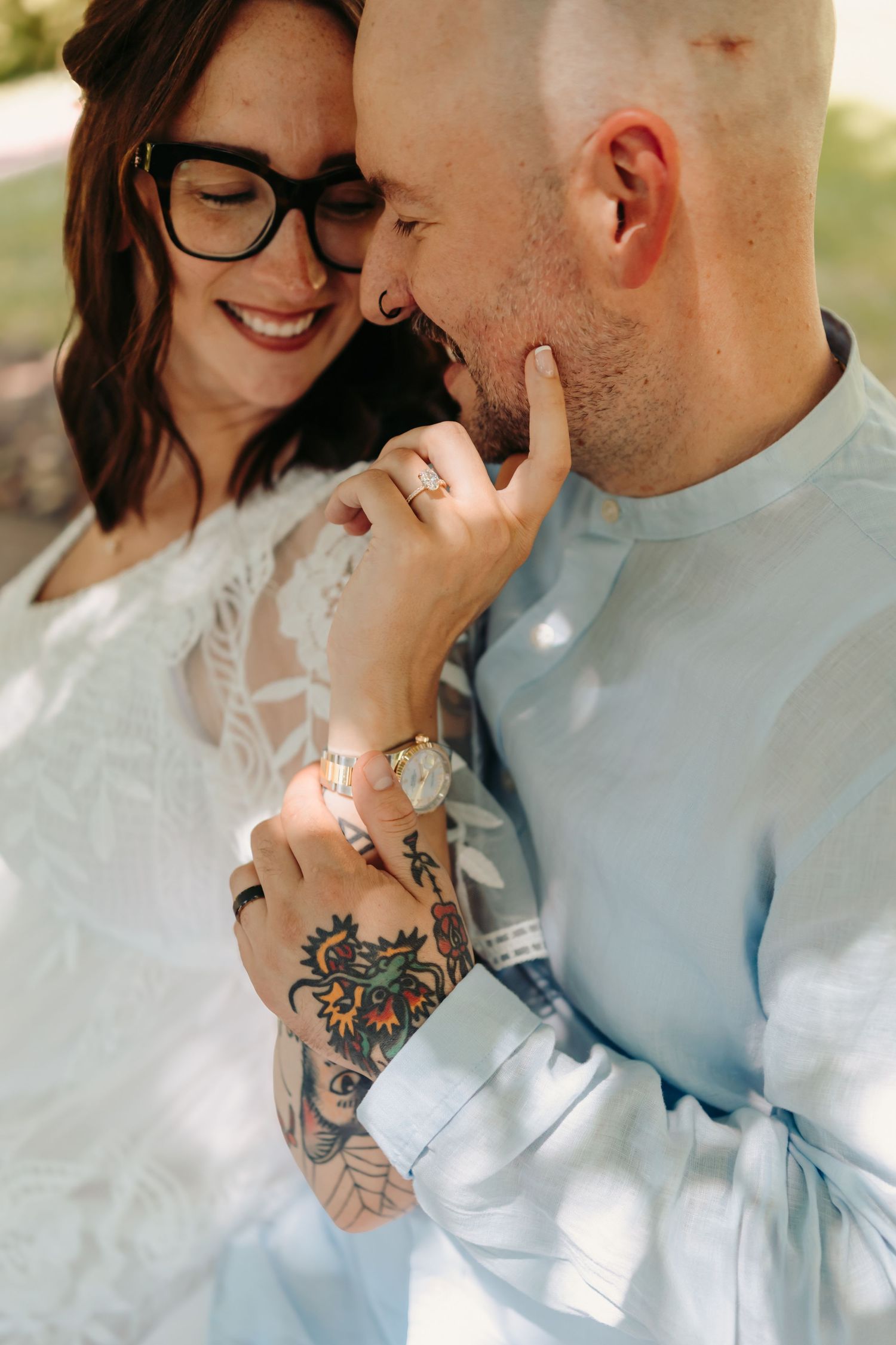 Intimate close-up of a couple embracing, showing colorful floral tattoo on arm and an engagement ring.