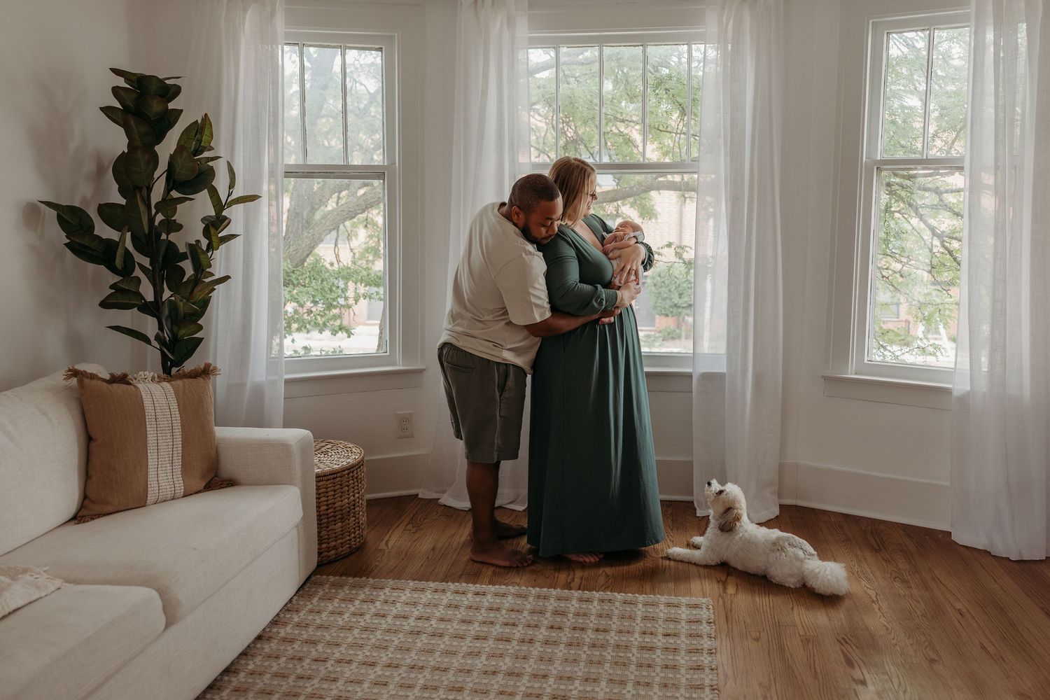 A couple shares an intimate moment in a bright corner living room with large windows and a white cat lounging nearby.