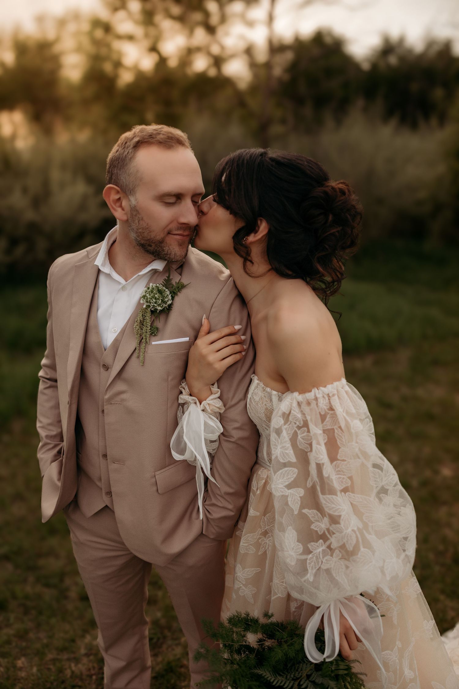 A romantic sunset wedding photo showing a couple in beige and white attire sharing an intimate moment outdoors.