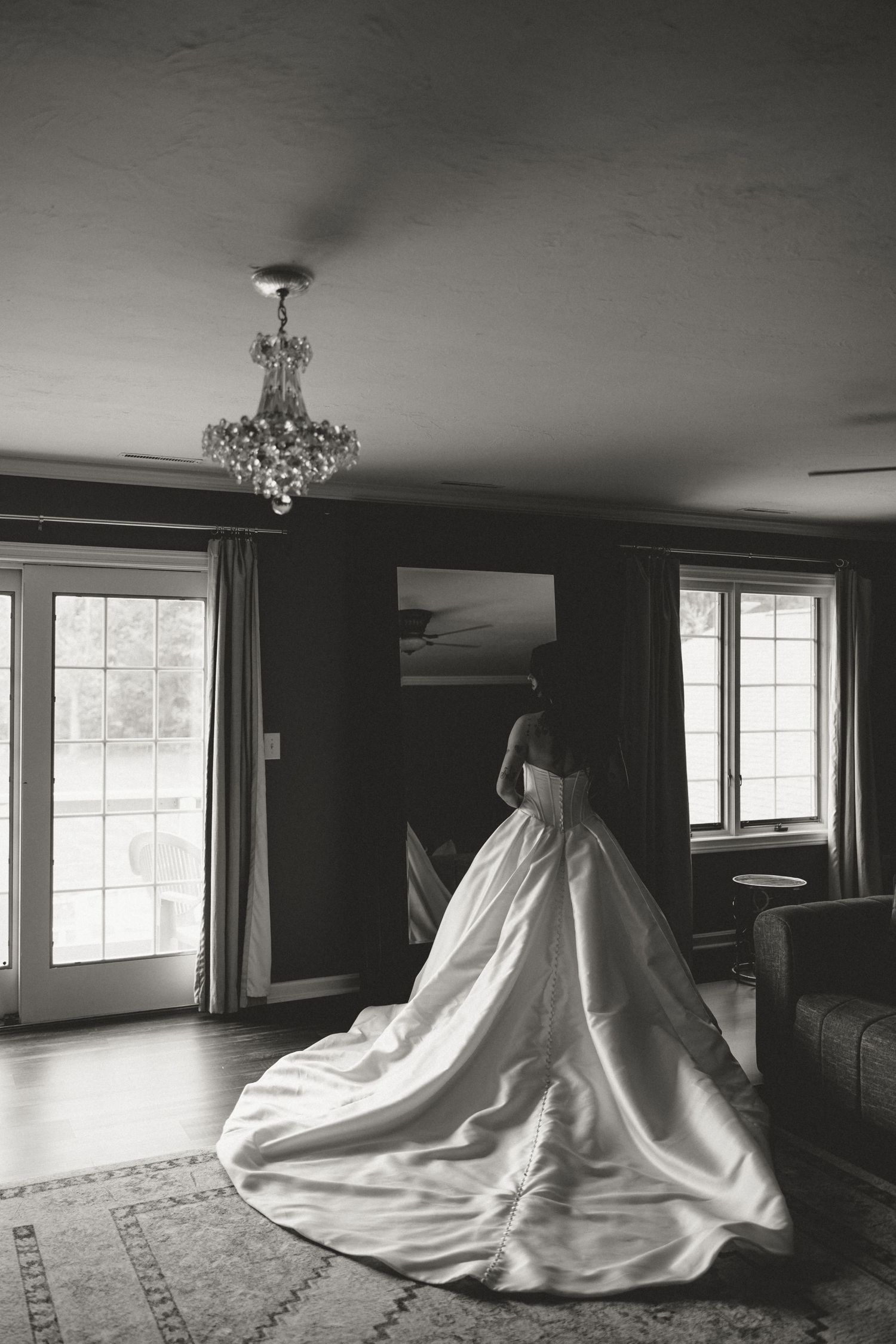 Elegant bride in a full ballgown wedding dress standing by windows in a black and white photo.