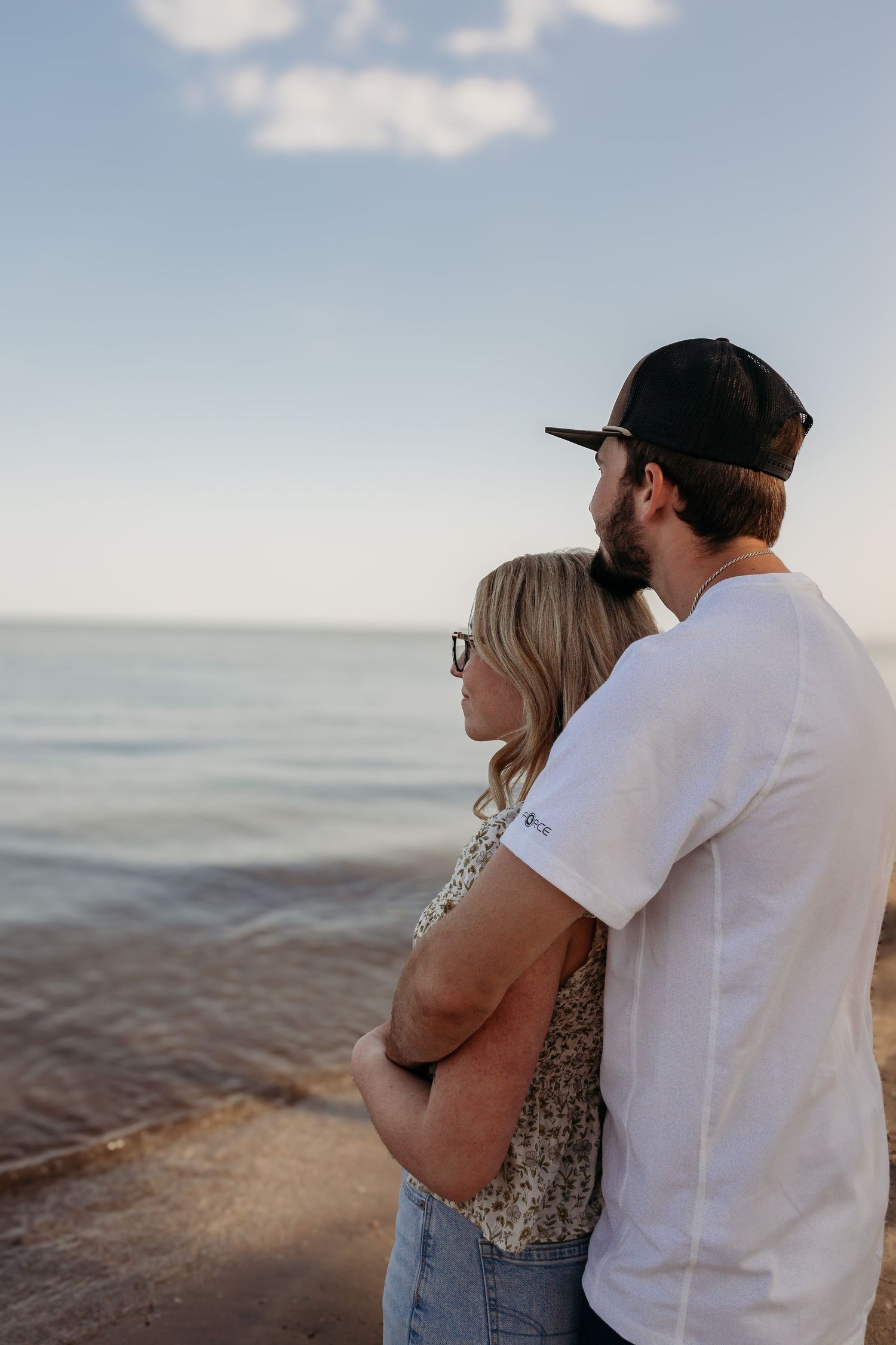 Couple embracing while watching sunset over calm ocean waters on a peaceful evening.