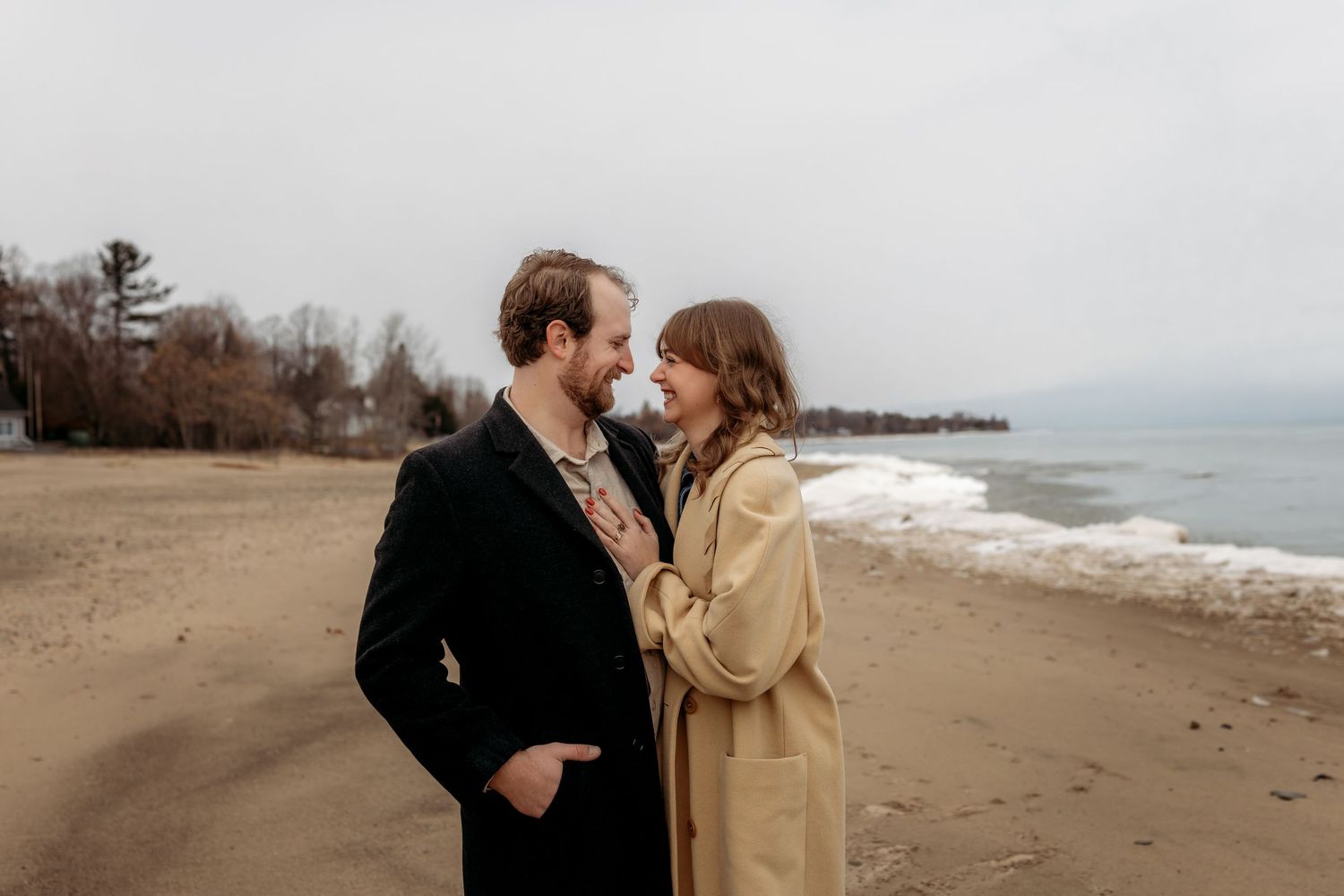 Romantic beach engagement photos showing a couple against a cloudy winter shoreline background.