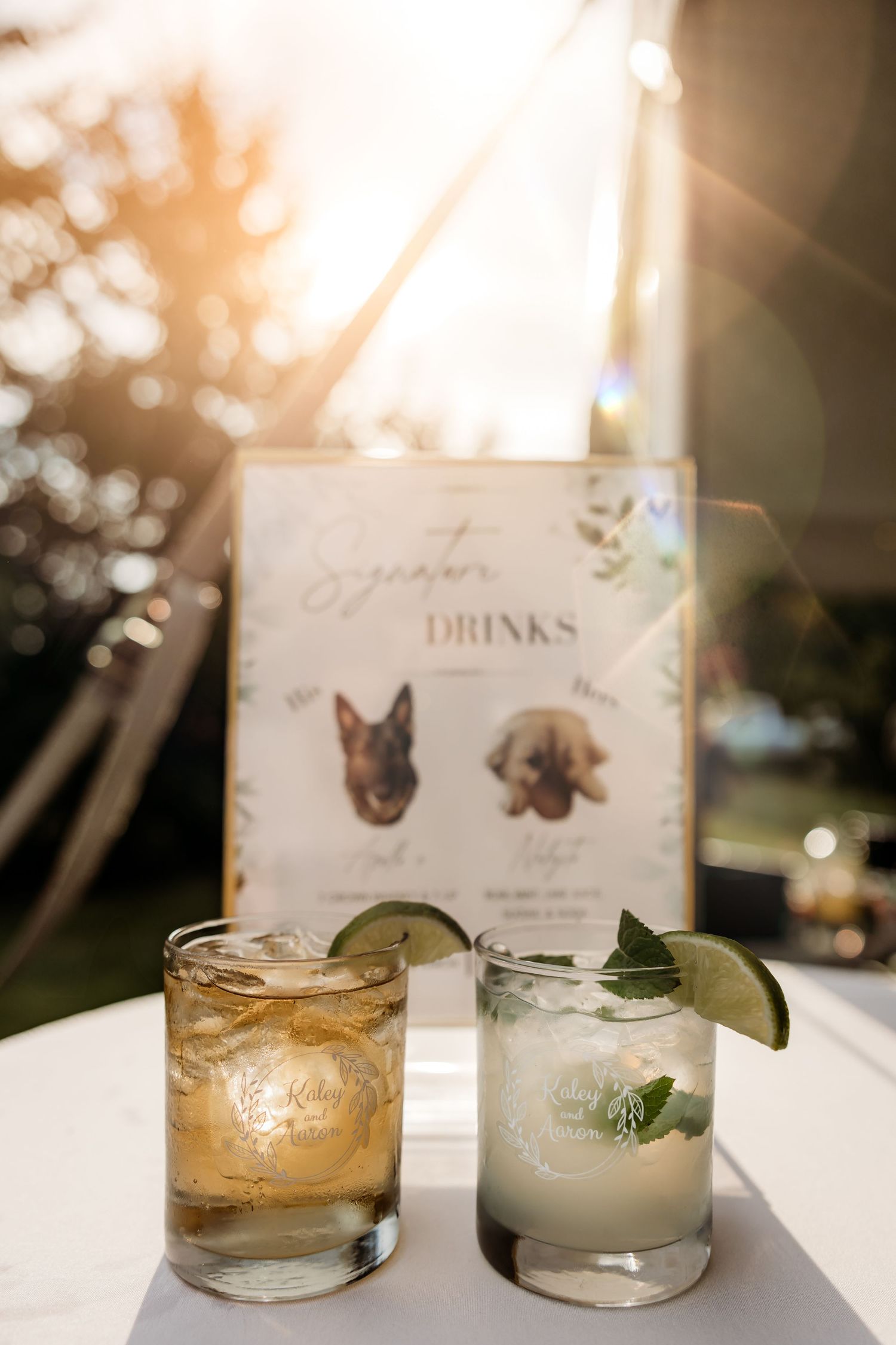 Elegant cocktail menu and drinks display at sunset with glowing bokeh lights and crystal glasses on white table.