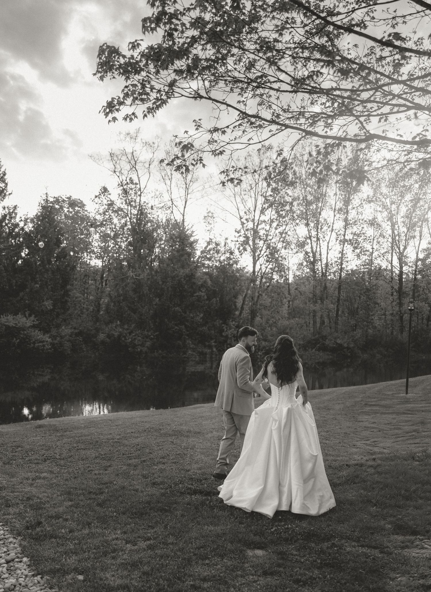 Bride and groom holding hands walking through a scenic wooded landscape in black and white.