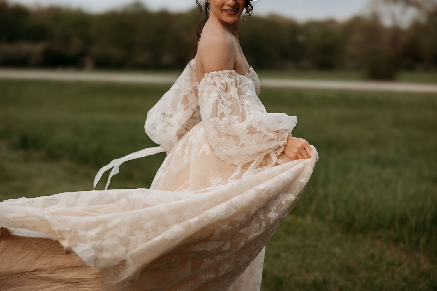 A wedding dress flowing gracefully in the wind across a grassy field in warm sunset lighting.