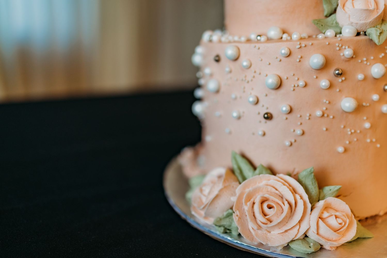 Close-up of elegant wedding cake decorated with peach roses and silver sugar pearls in a modern design.