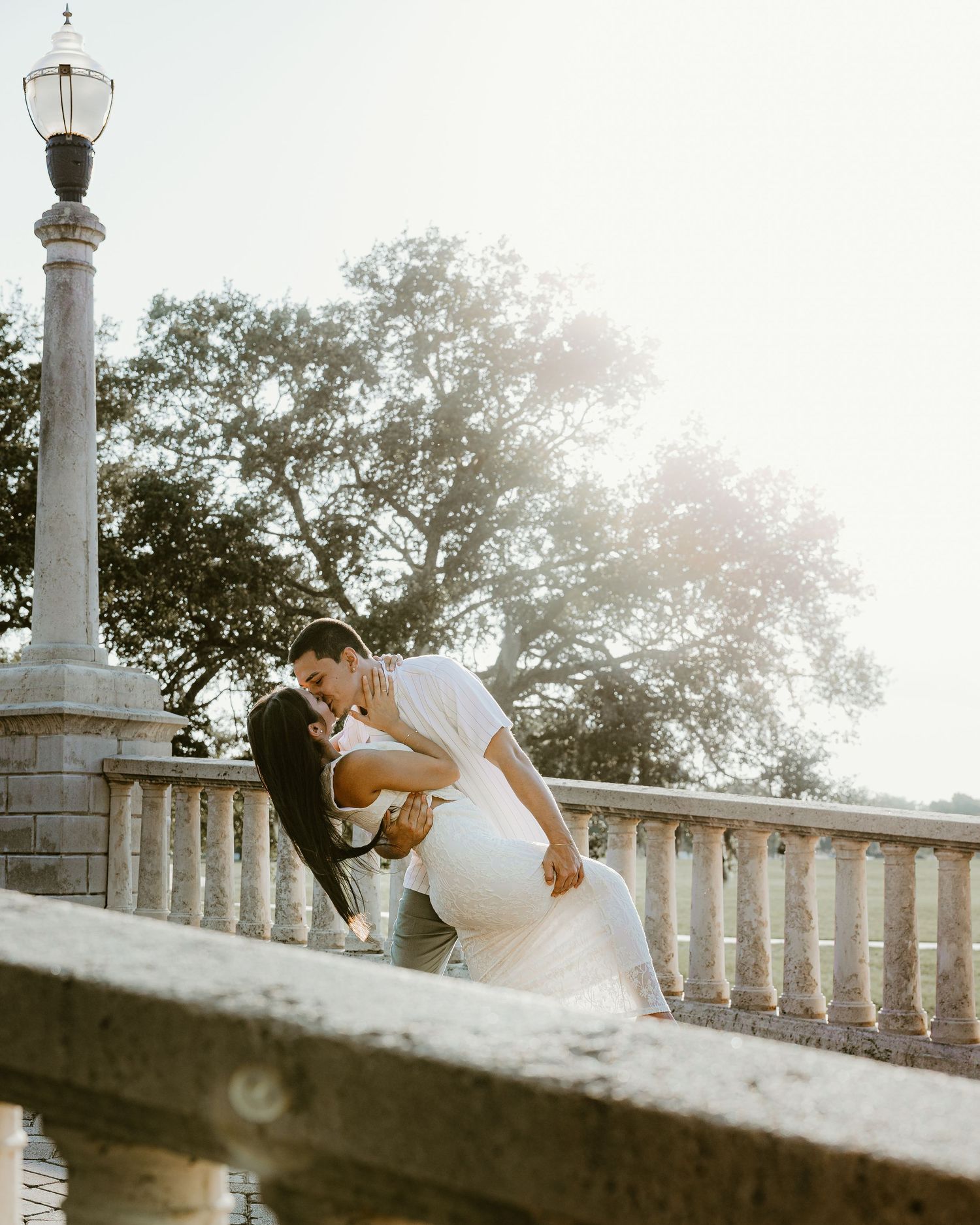 Romantic couple pose together on a stone balustrade at golden hour.