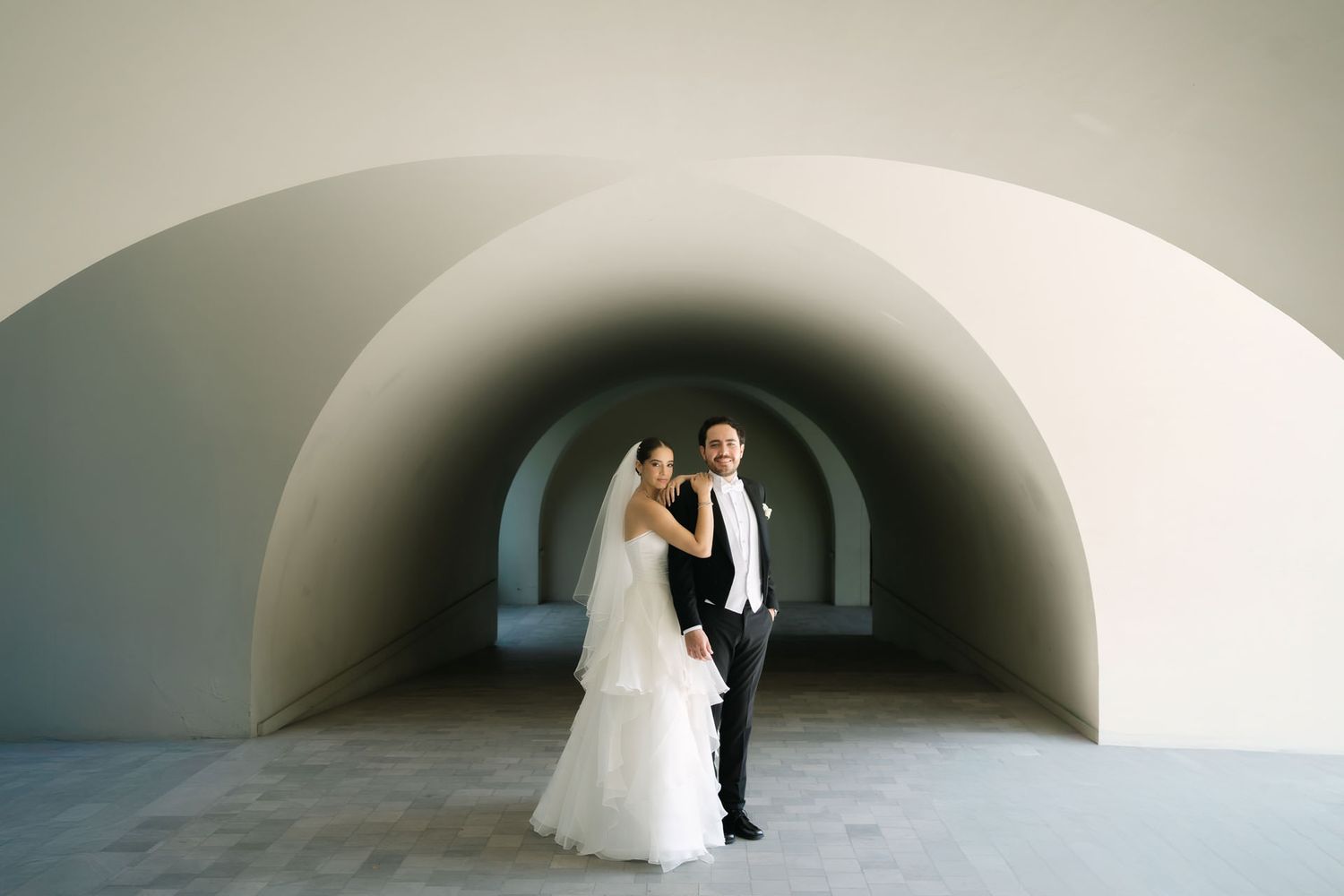 A series of wedding photos showing couples posing in an arched white corridor with soft lighting.