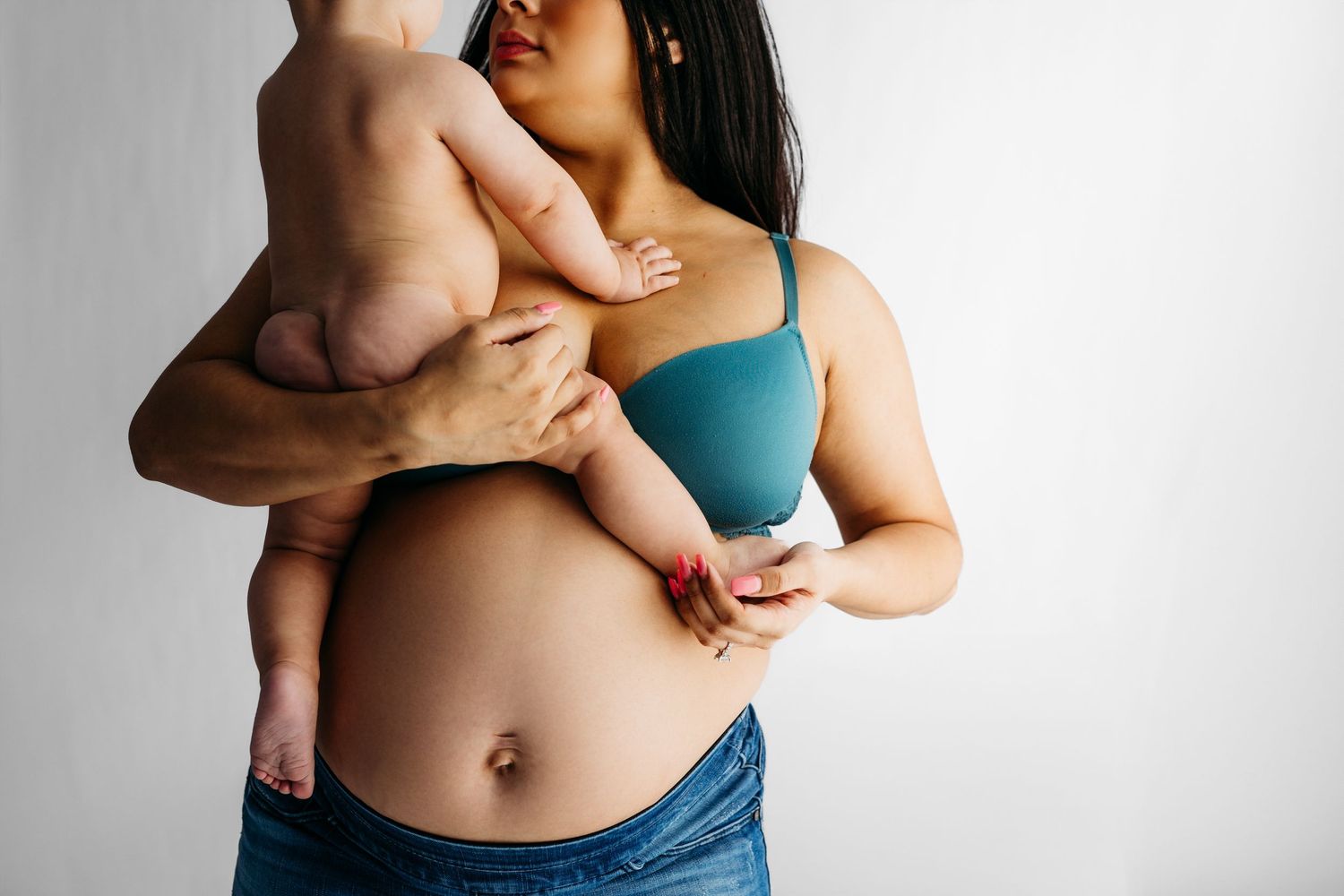 A tender moment shows someone holding a baby against their chest while wearing a teal tank top and denim.