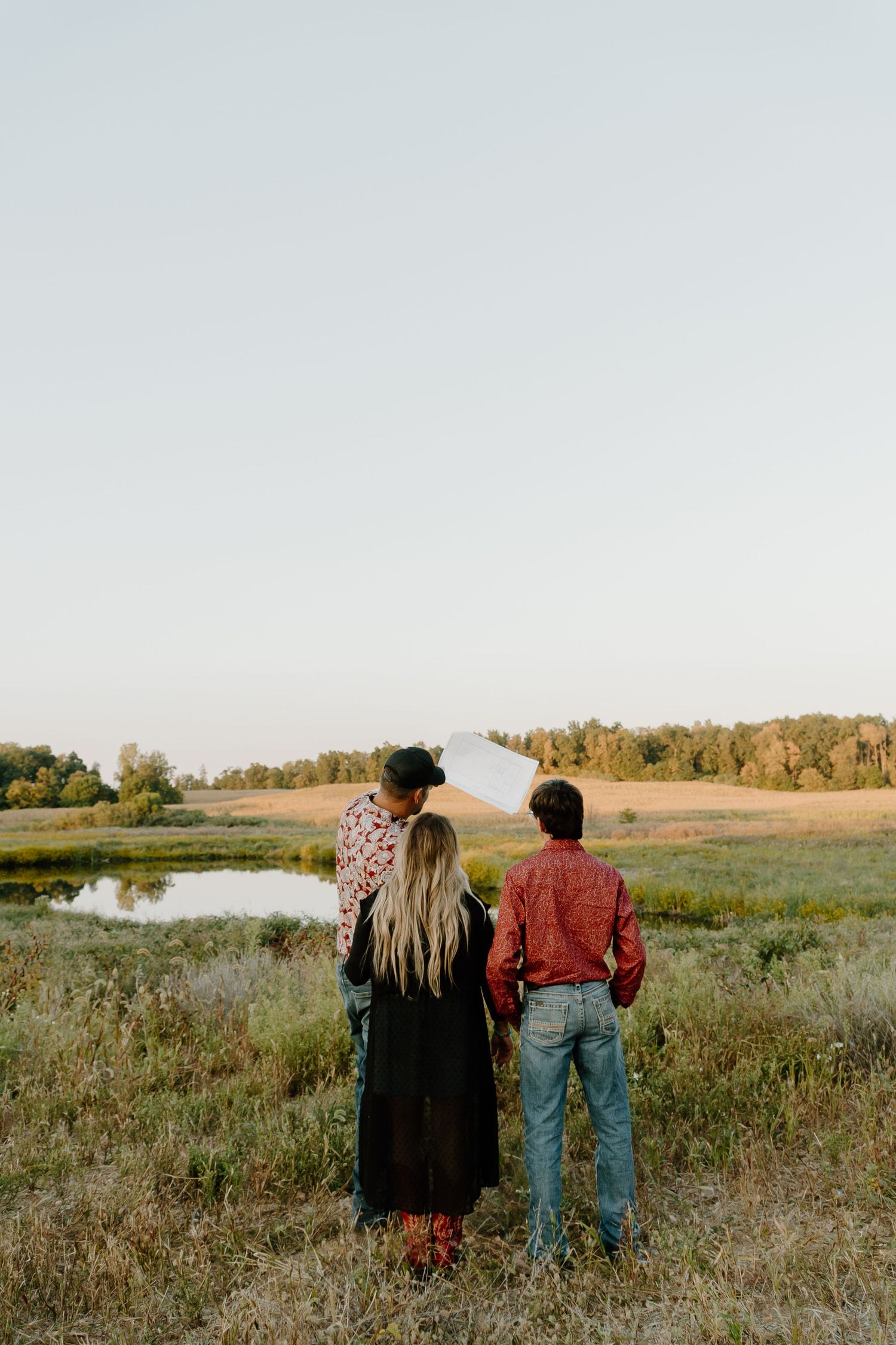 A couple walks through a scenic meadow at sunset overlooking a peaceful pond in the countryside.