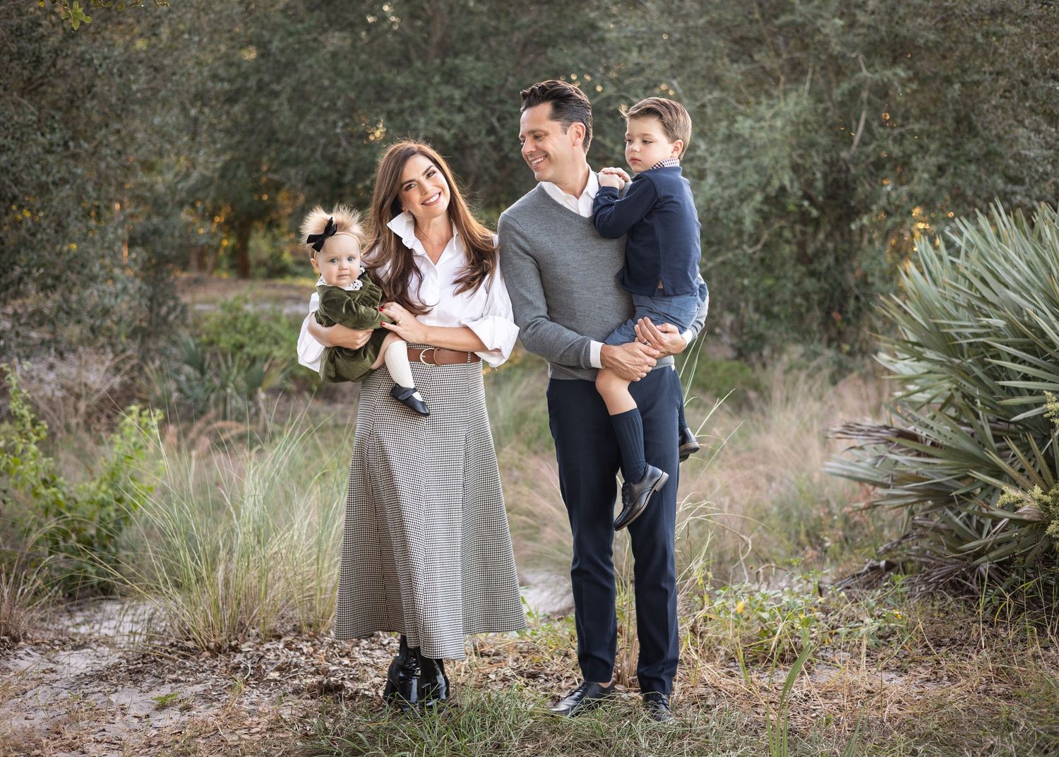 A family standing in a natural outdoor setting, with a man, woman, and two young children, one of whom is being held.