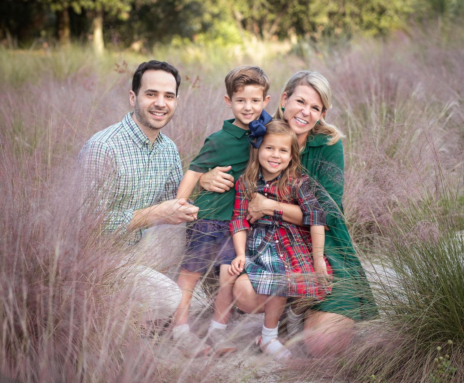 A happy family of four, including a mother, father, and two children, sitting together in a grassy field.