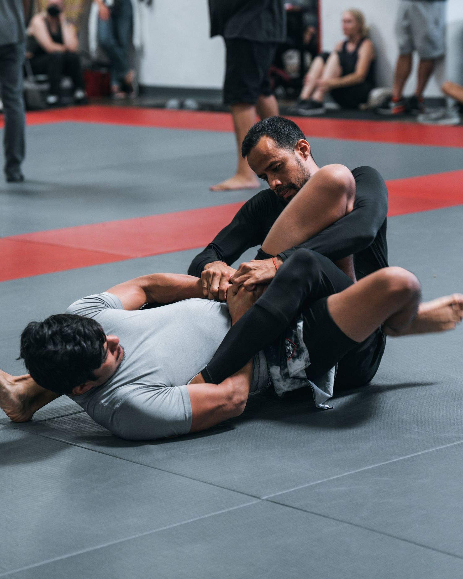 Martial arts practitioners demonstrating grappling moves on a gray mat.