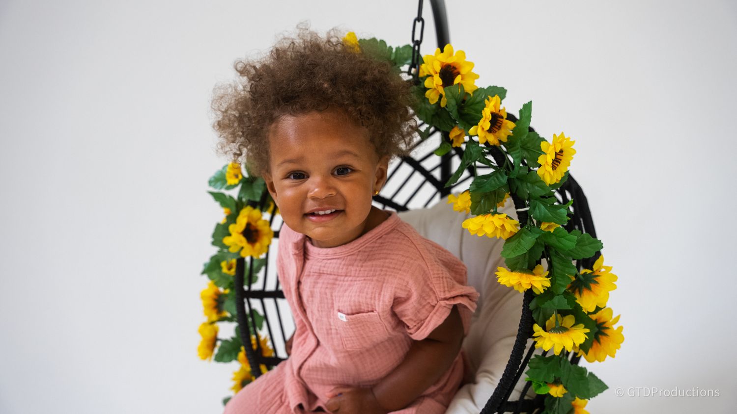 A happy child wearing pink surrounded by decorative yellow flowers.