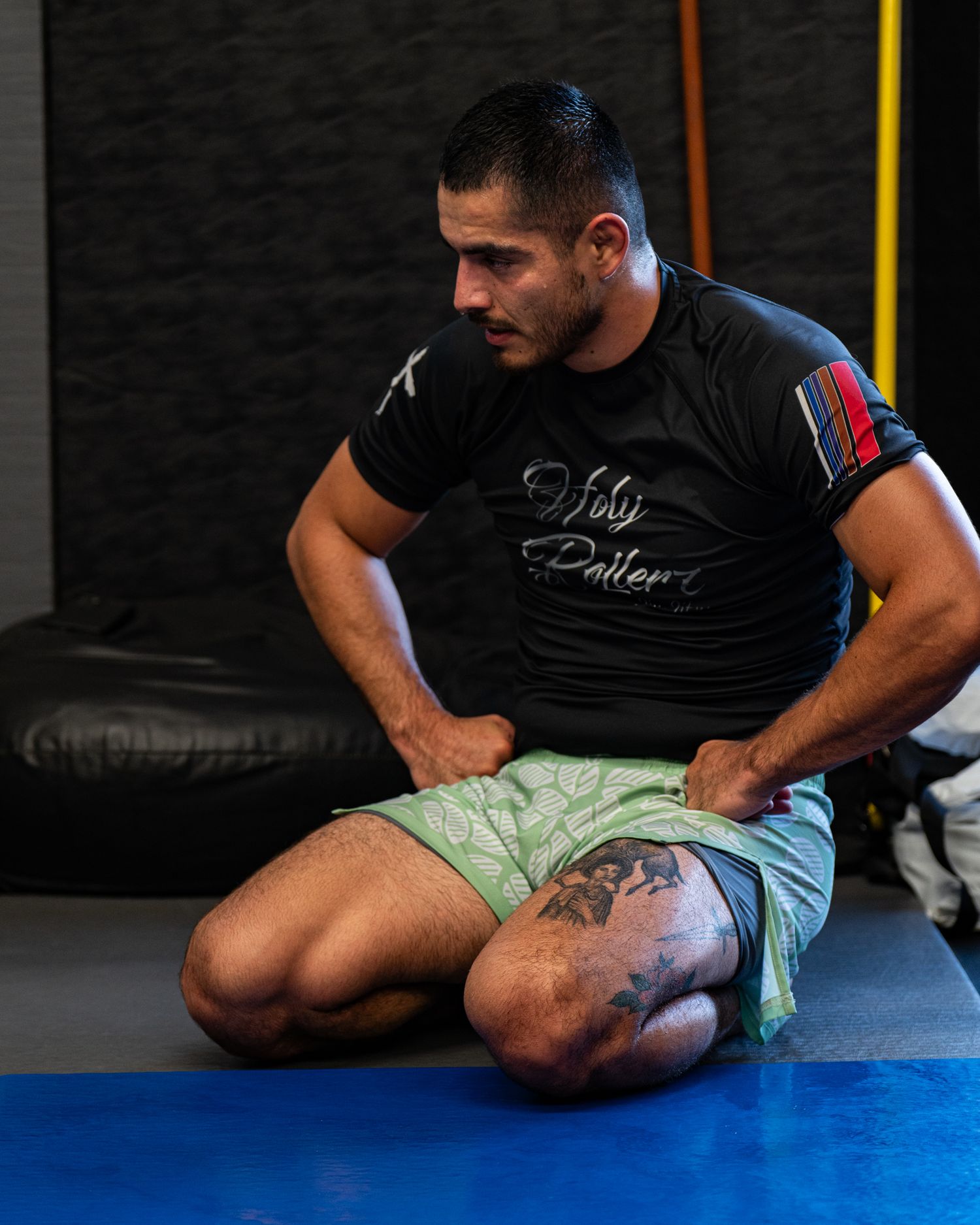 Athletes practicing ground techniques on blue training mats in a gym.