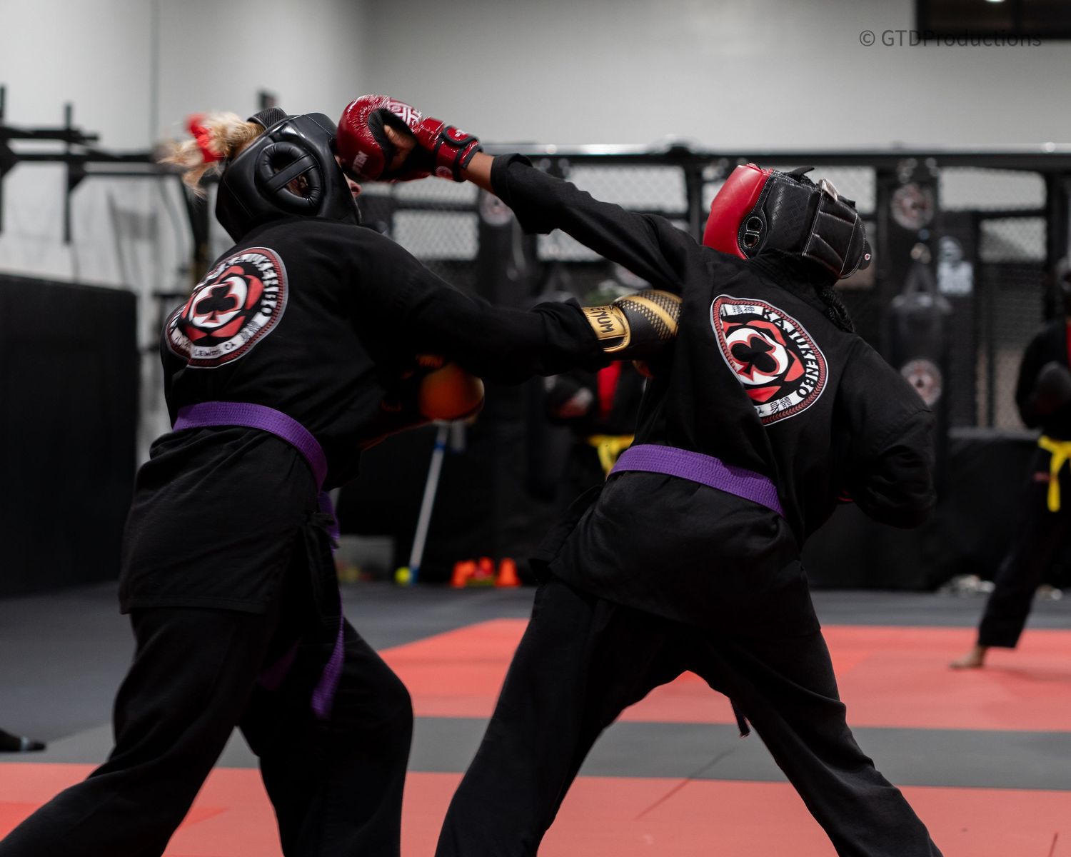 Students practicing martial arts moves on red and black mats.