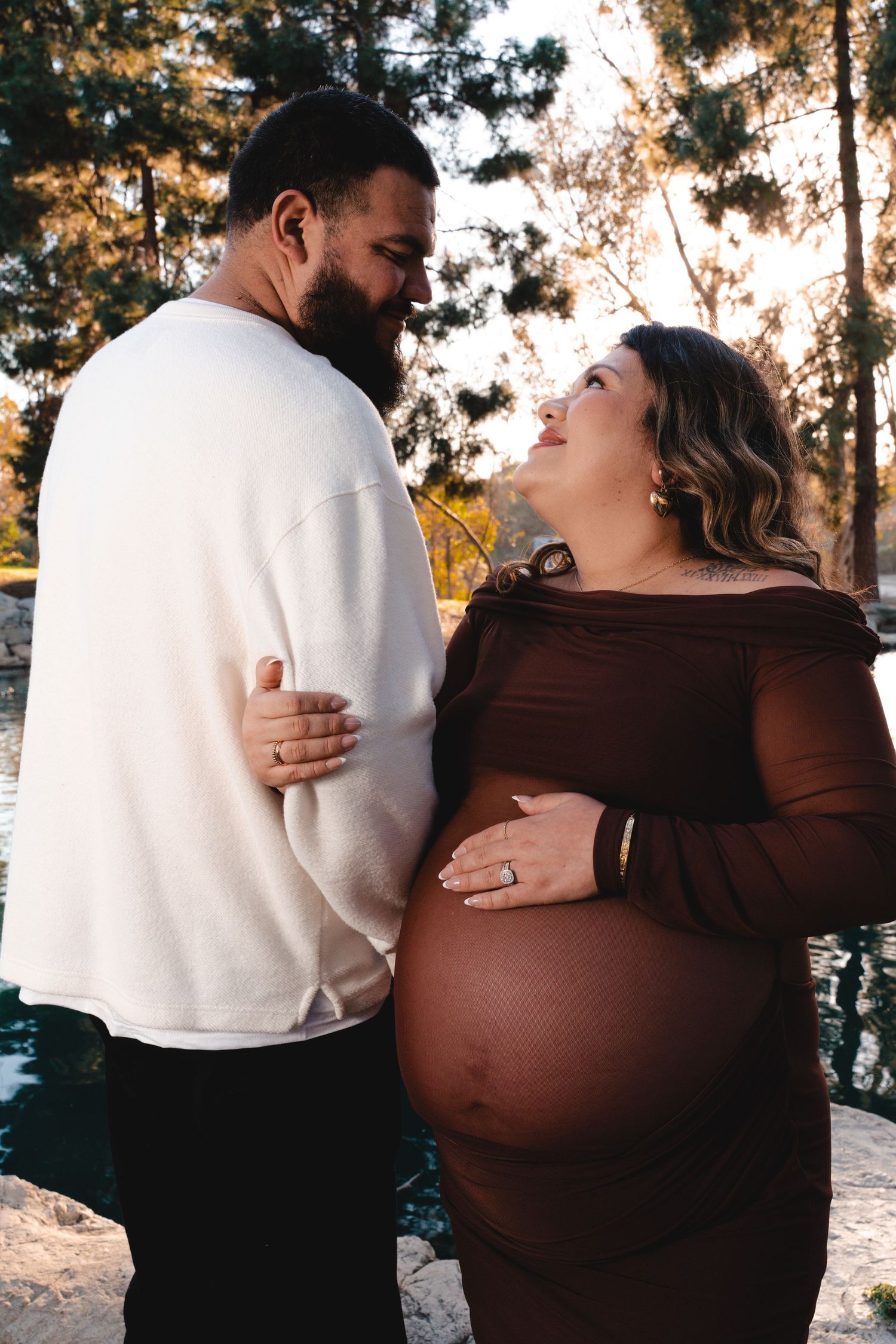 A couple embraces during an outdoor maternity photo session at sunset.