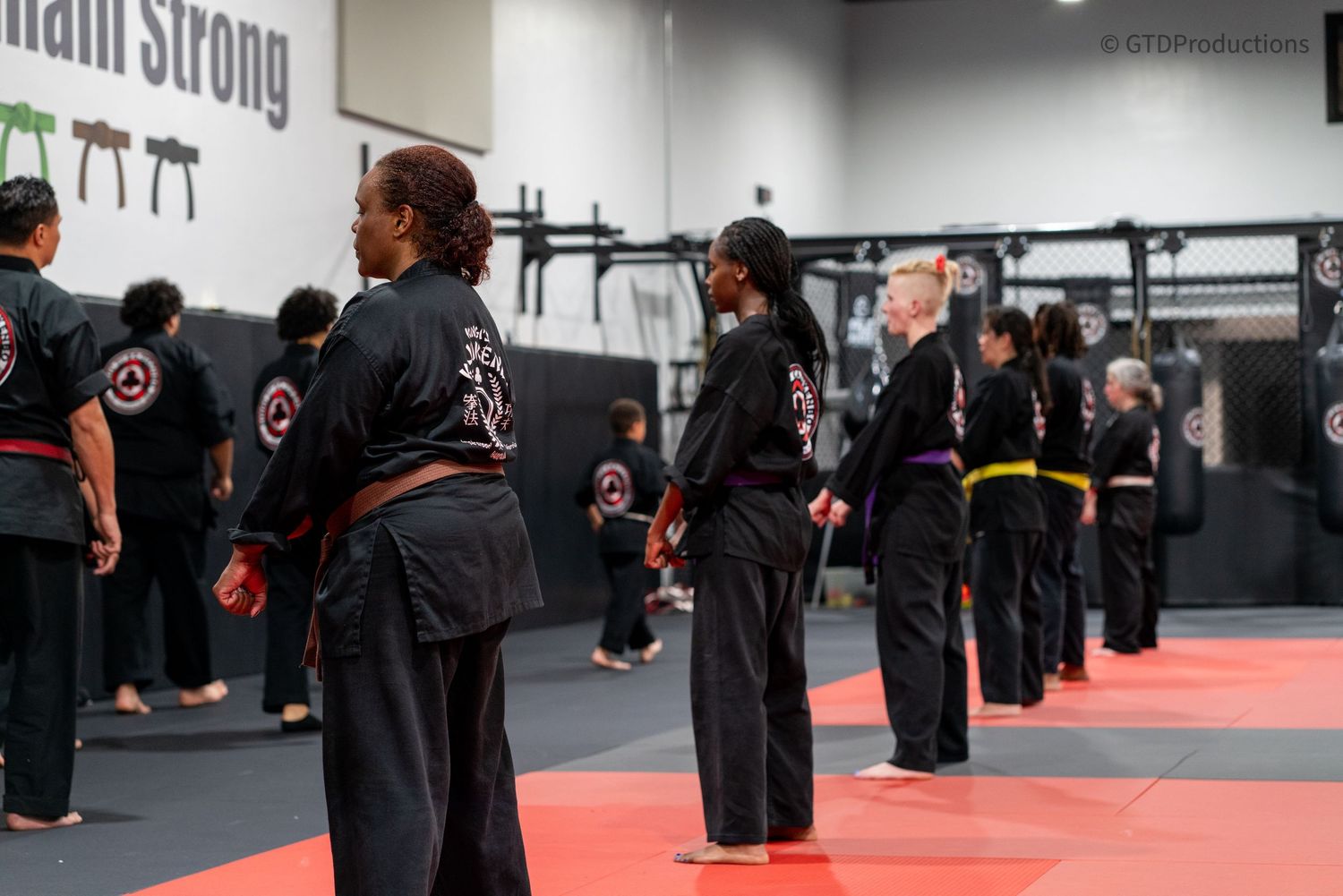 Martial arts students practicing in a training facility with red mats and black uniforms.
