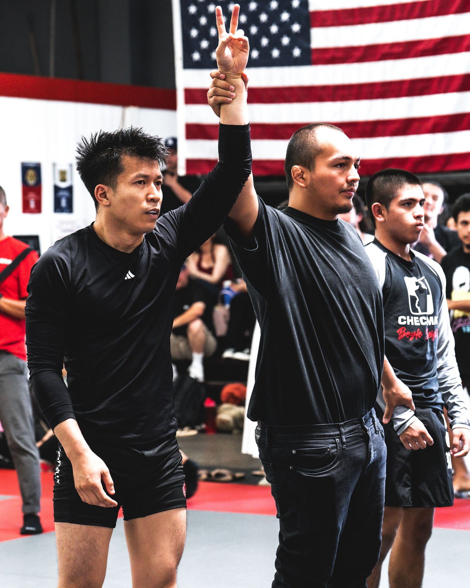 Athletes training in black uniforms with an American flag backdrop in a martial arts studio.