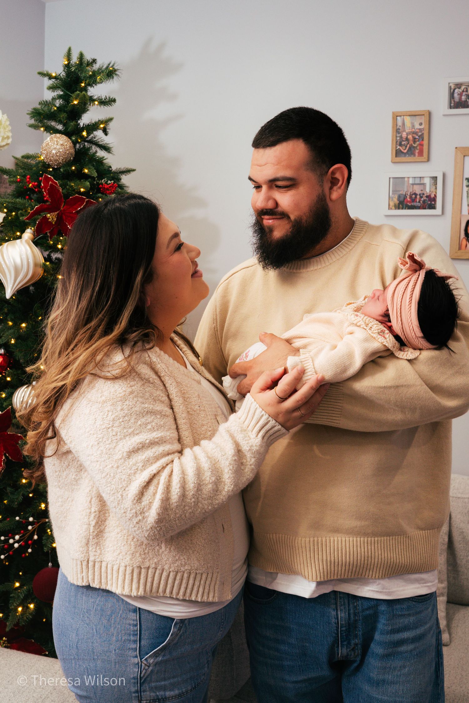 Playful couple in matching cream sweaters pose by Christmas tree.