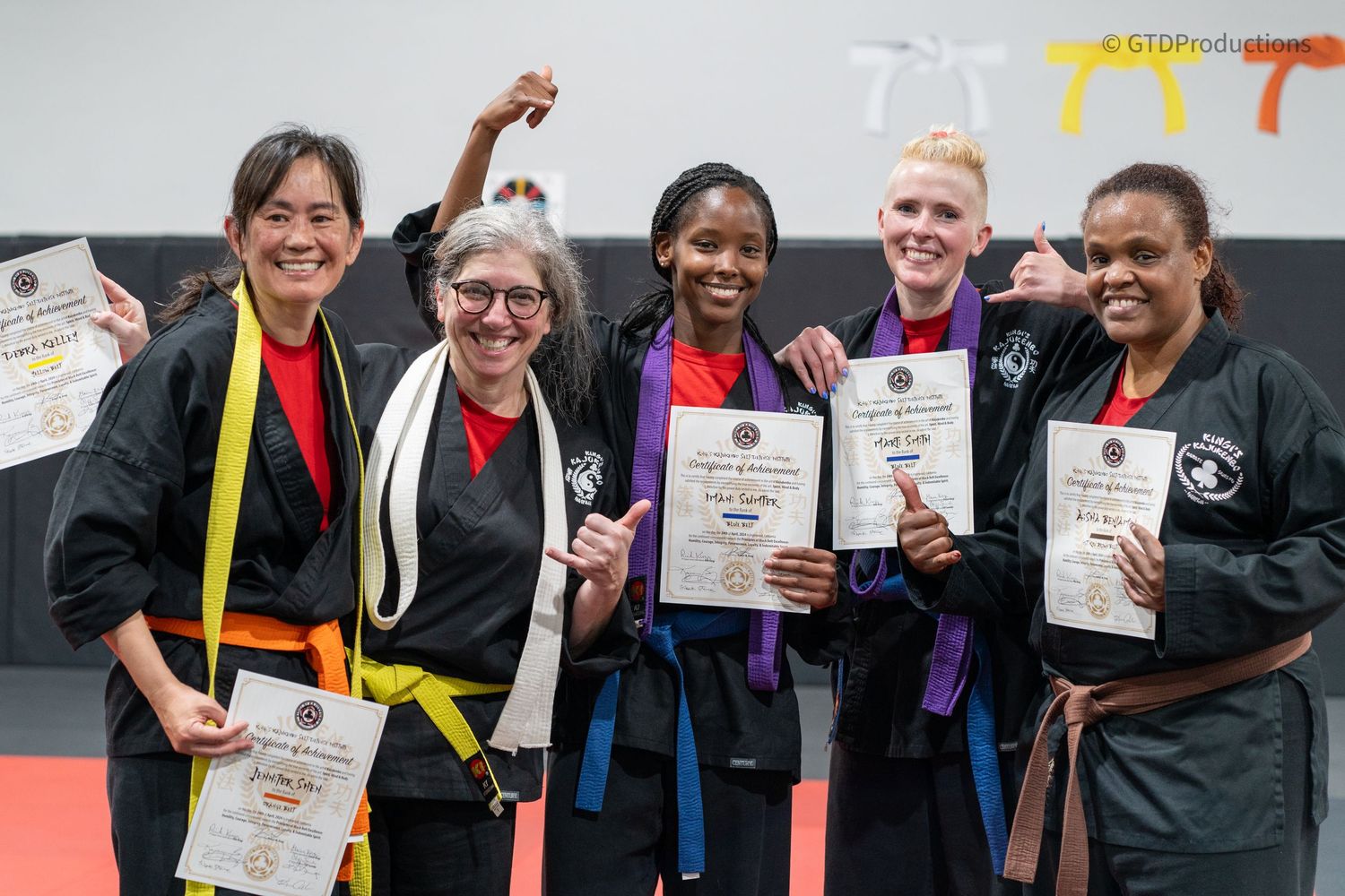 Group of martial arts students displaying certificates and colored belts after a promotion ceremony.
