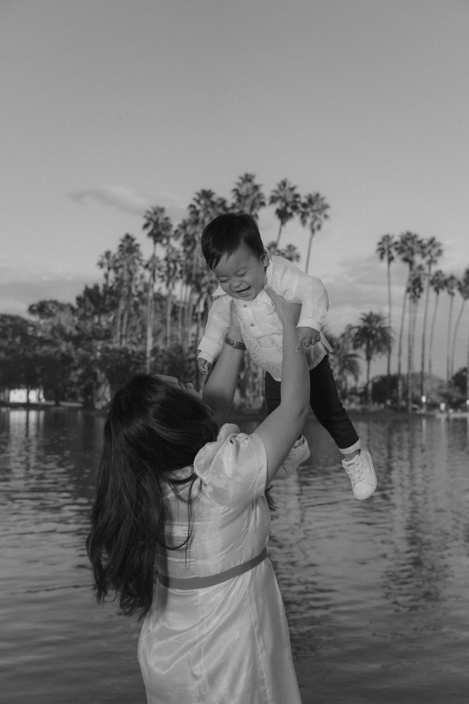 Black and white family photos taken in front of a scenic waterfront with palm trees.