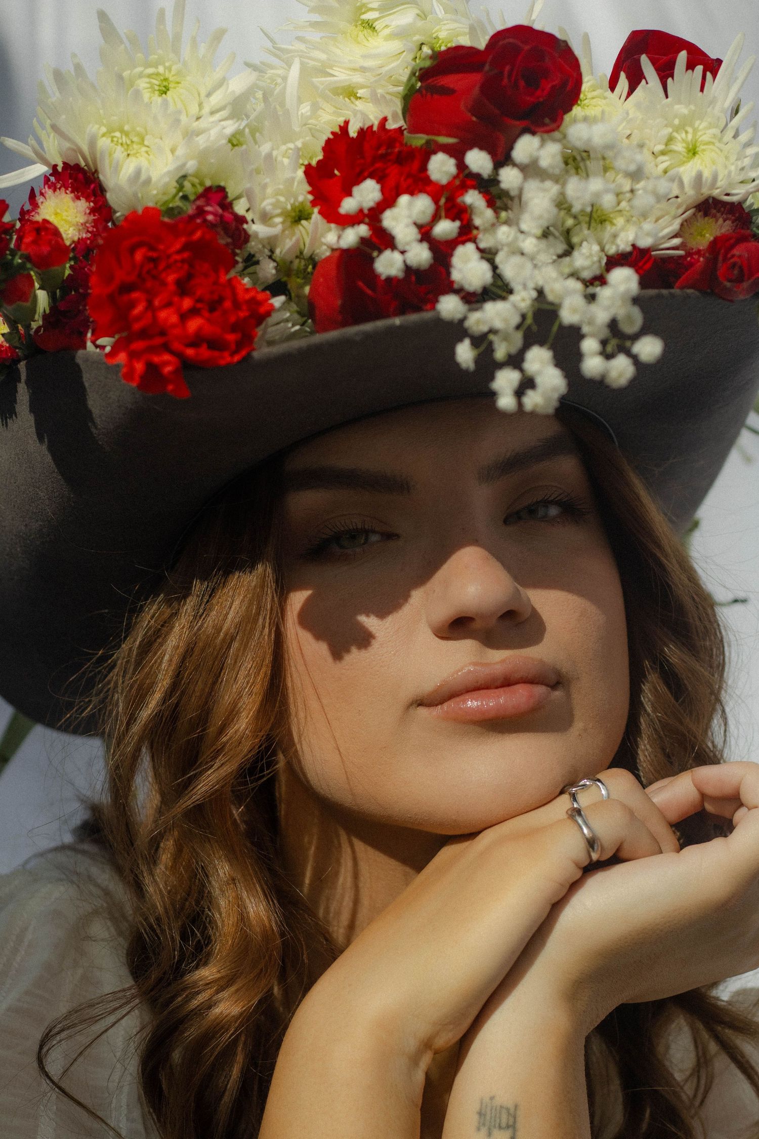 A floral crown adorned with red roses and white baby's breath creates a romantic bridal look in natural sunlight.