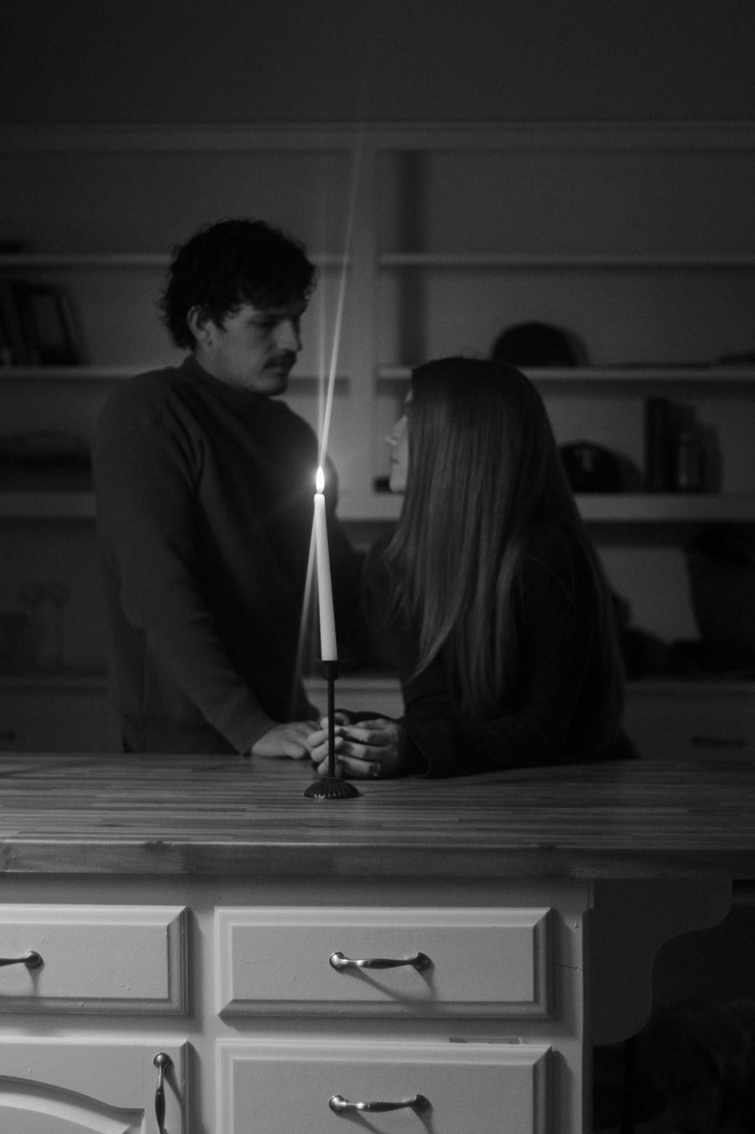 Silhouettes of people near candlelight in a dimly lit room with white cabinets.