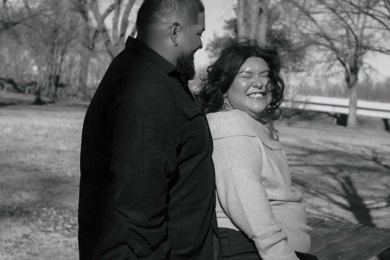 A black and white photo of a couple sharing a happy moment in a park setting.