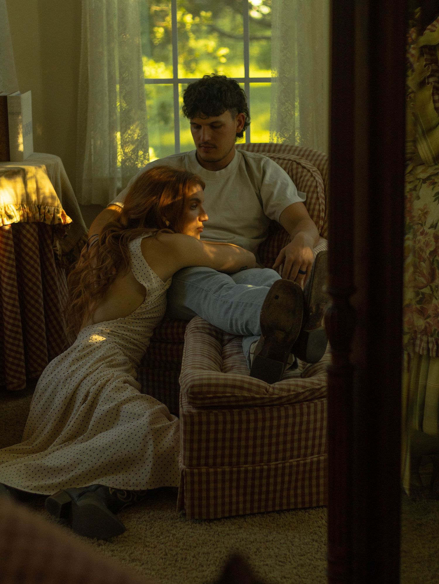 A couple relaxes together in a cozy armchair bathed in golden sunlight by a window.
