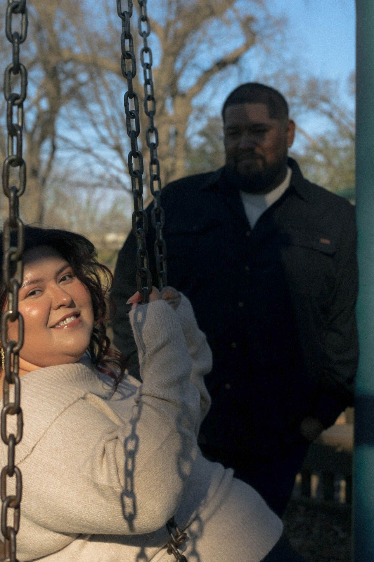 Person smiling while swinging at a park playground on a sunny winter day.