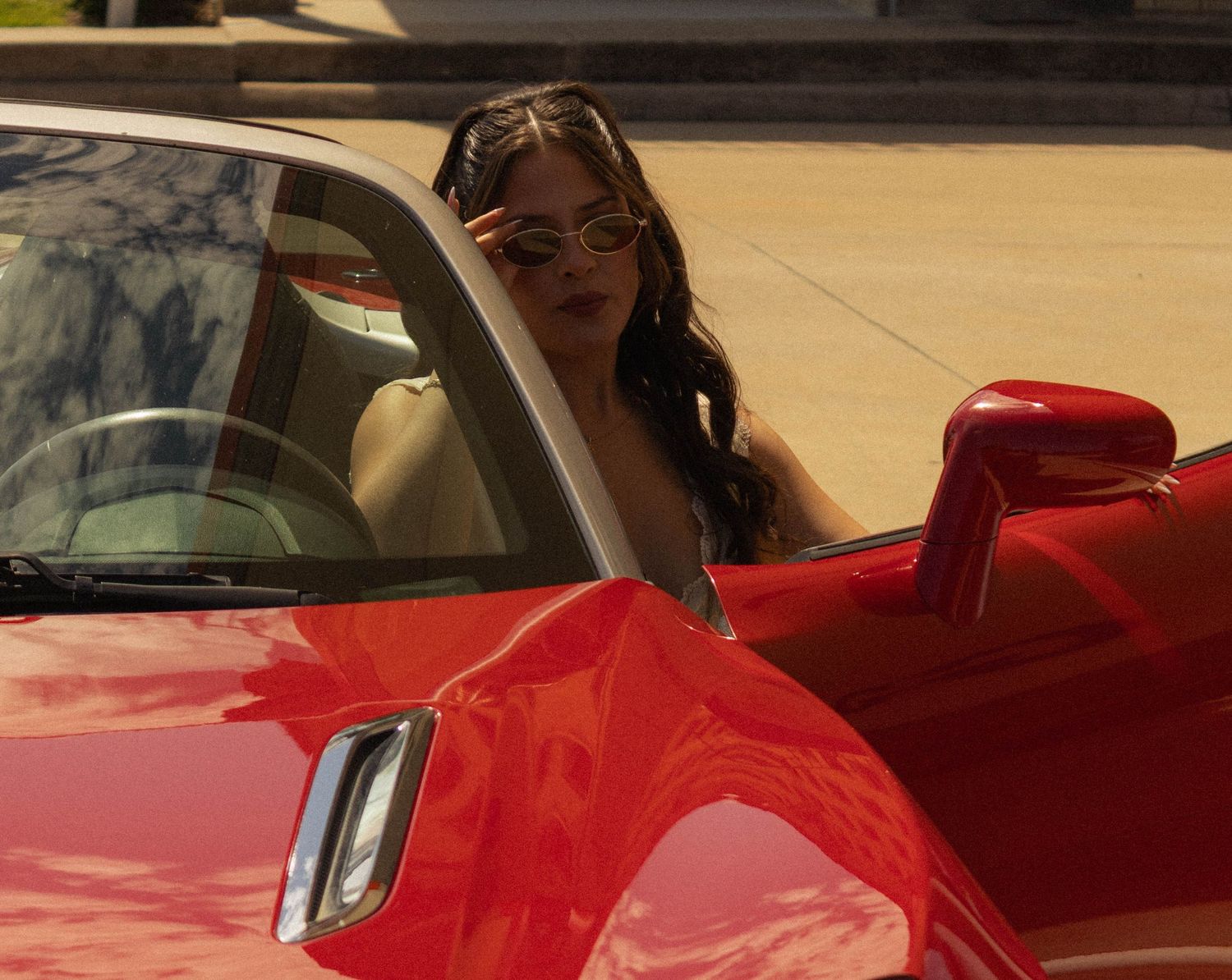 Woman with sunglasses stepping into a red convertible sports car on a sunny day.