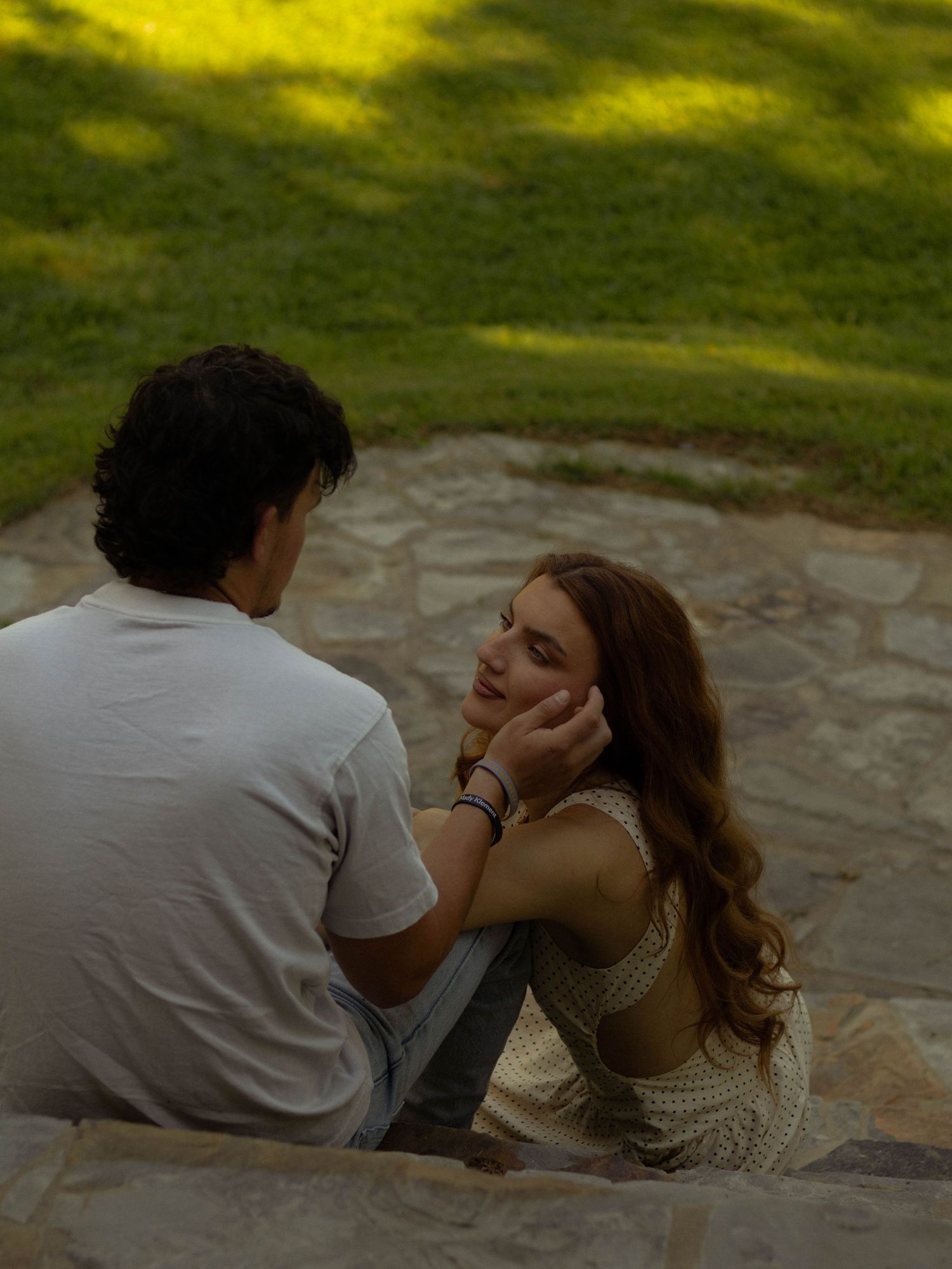 Young couple sitting together on stone steps in a lush green park sharing an intimate moment.