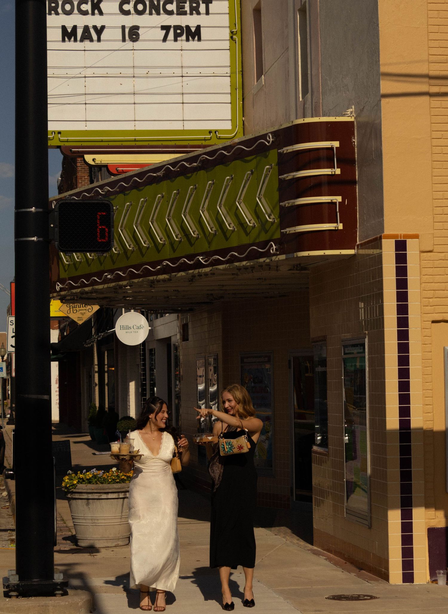 Two women stand outside a vintage theater marquee advertising a Rock Concert on May 16 at 7PM.
