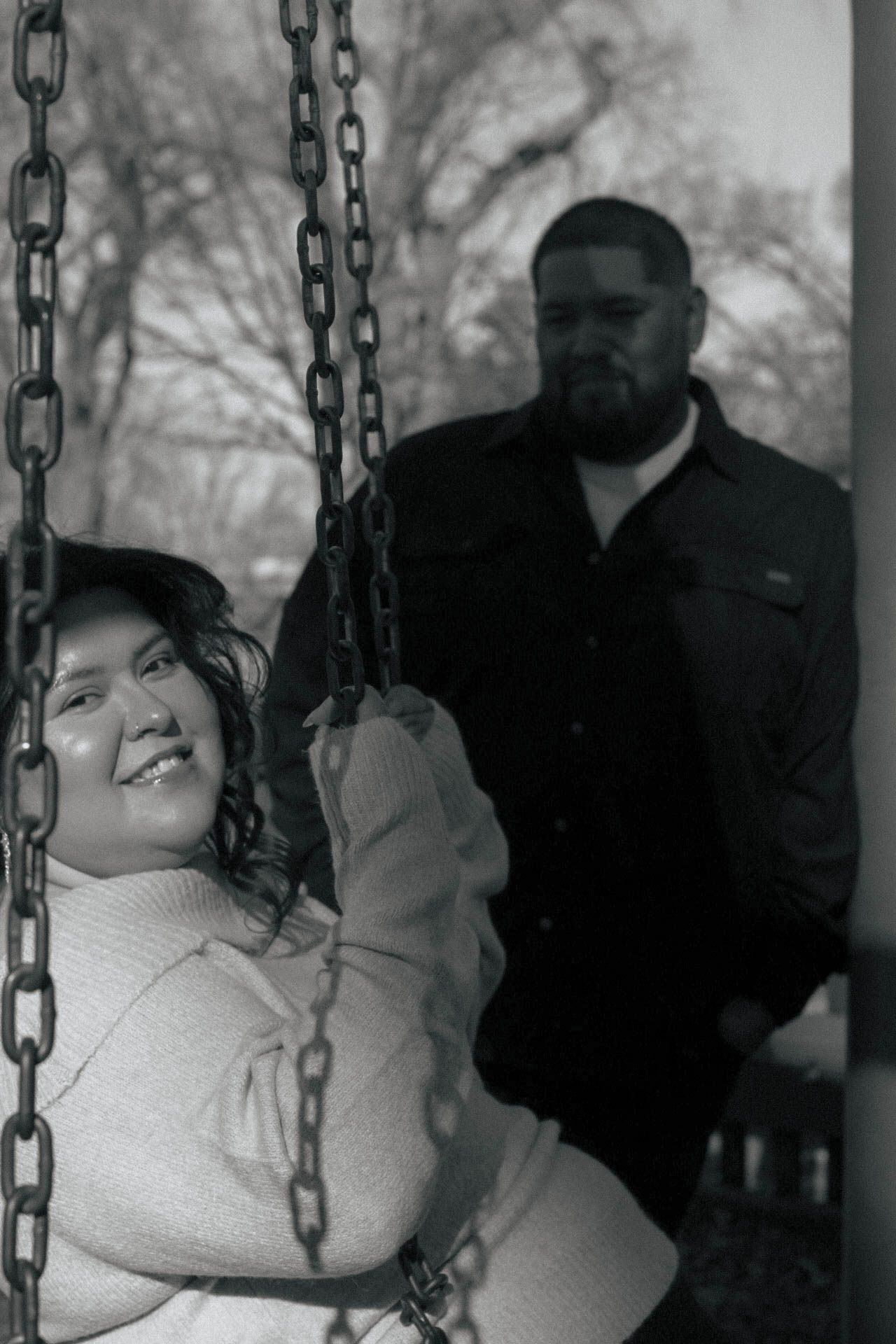 A couple shares a romantic moment on a swing set in black and white.