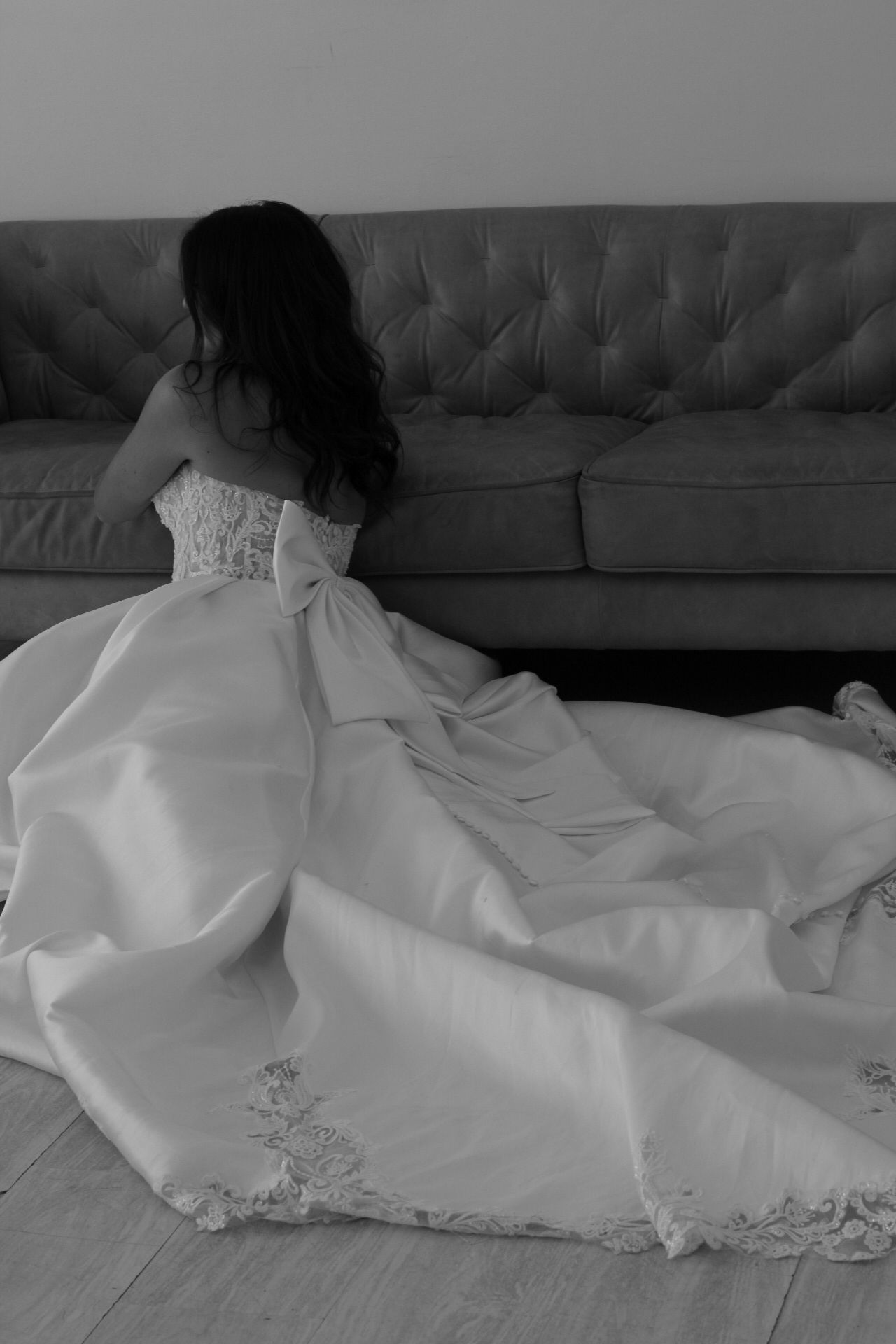 Wedding dress with intricate lace details spread across gray couch.