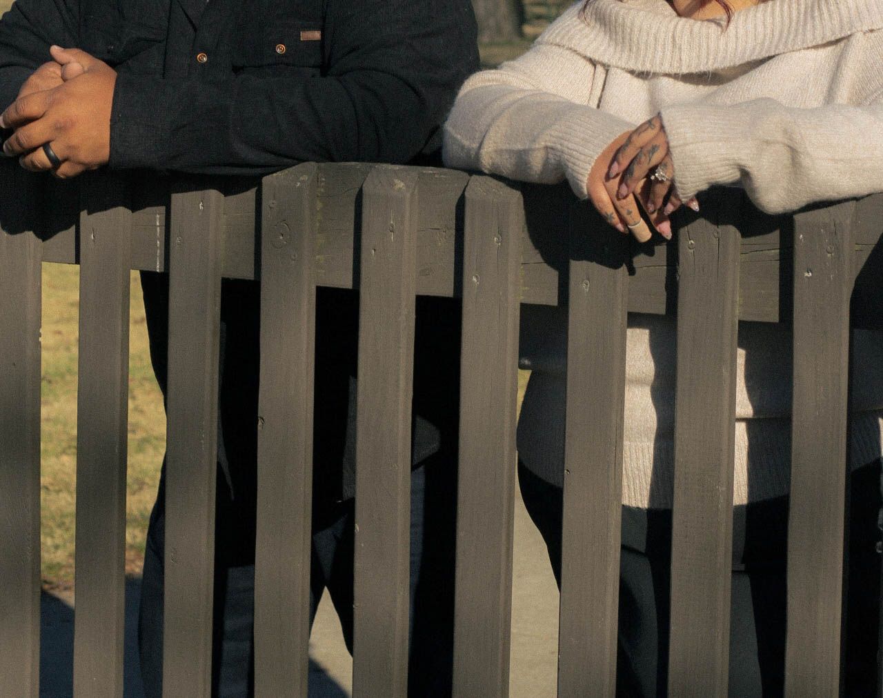 Close-up shot of hands resting on a wooden fence during a sunny day.