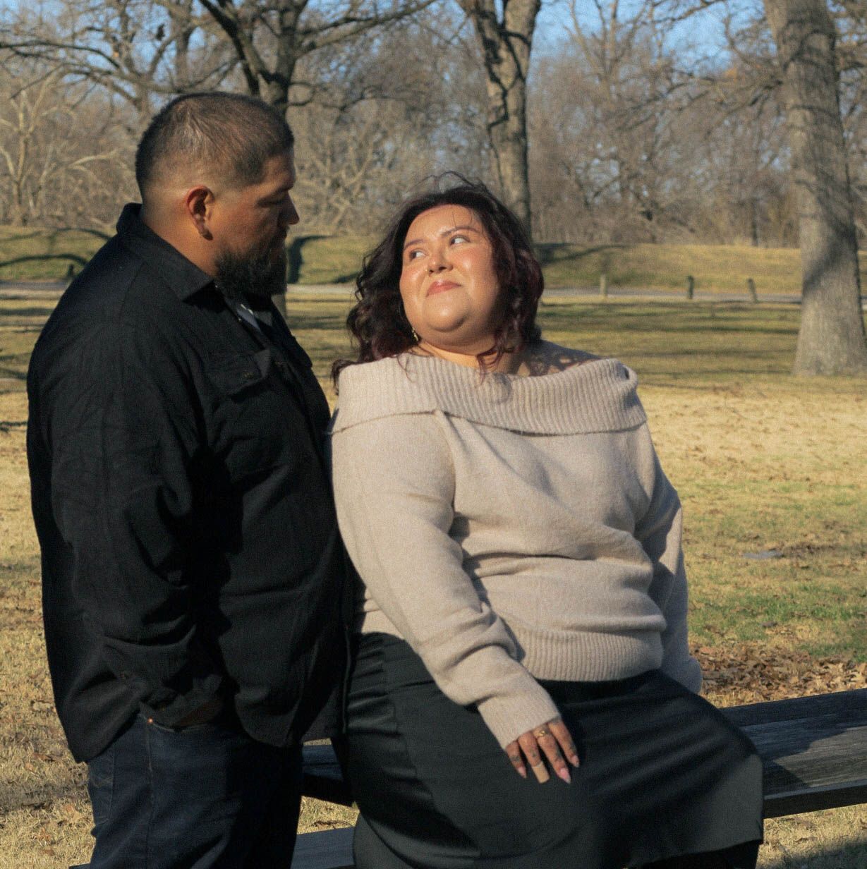 A couple sits close together outdoors during a winter day in the park.