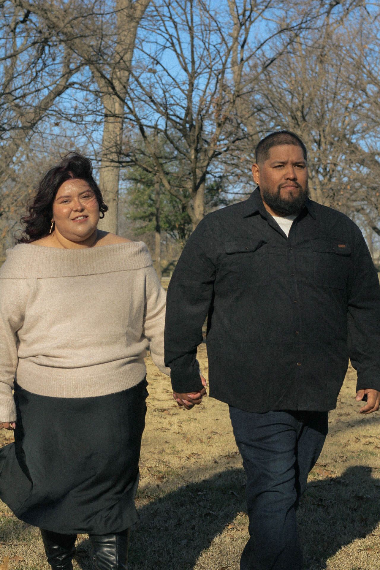 Two people in casual winter attire standing together in a grassy park area.